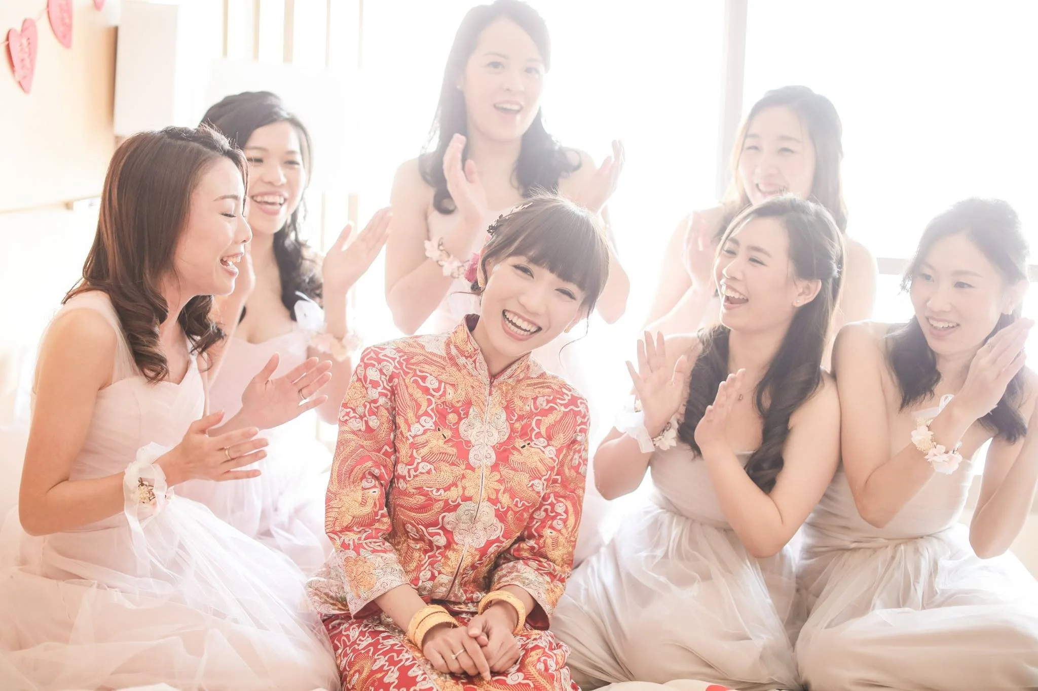 A group of women, with one in traditional Chinese attire, celebrating and laughing in a well-lit room.