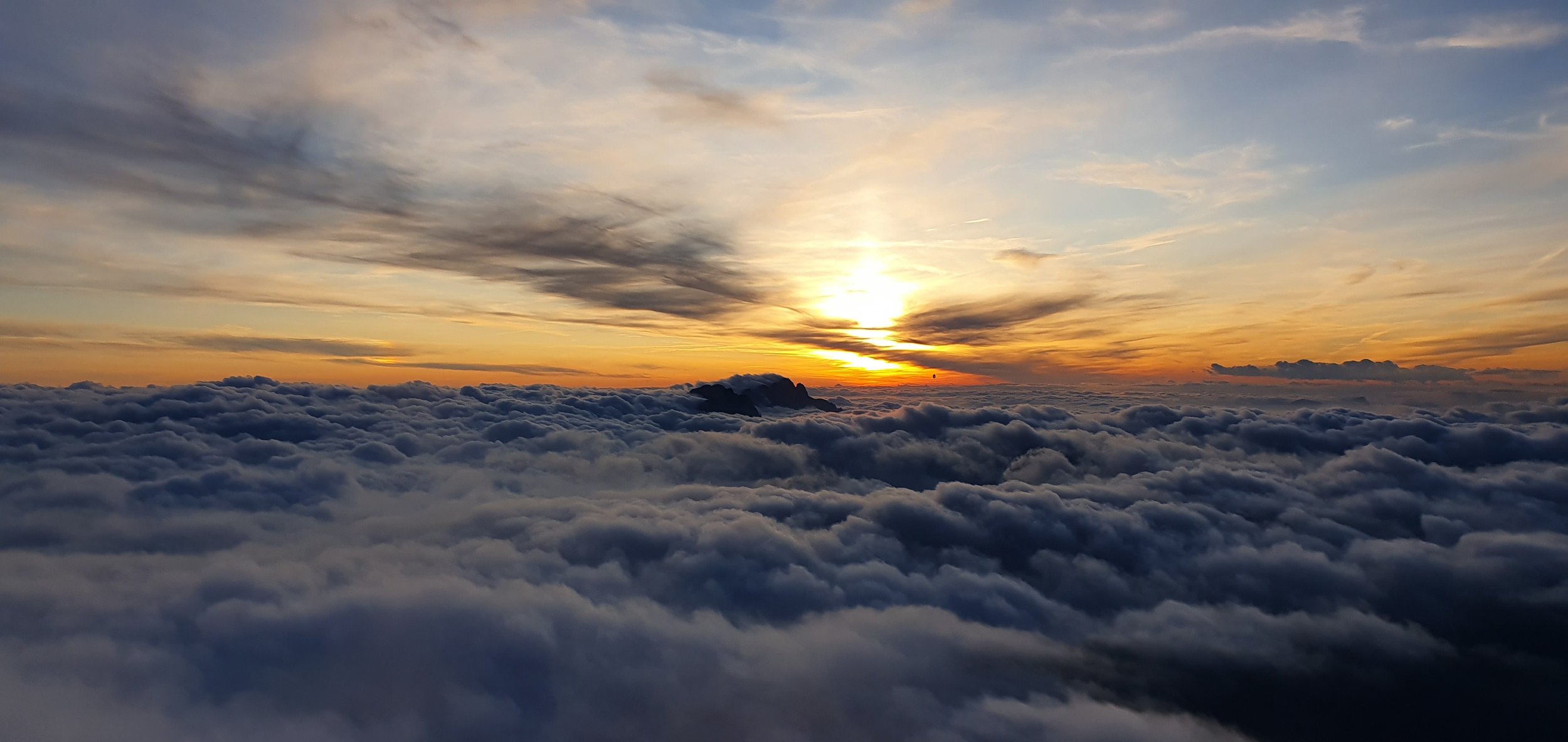 Sunset over a sea of clouds with a mountain silhouette and wispy clouds in the sky.