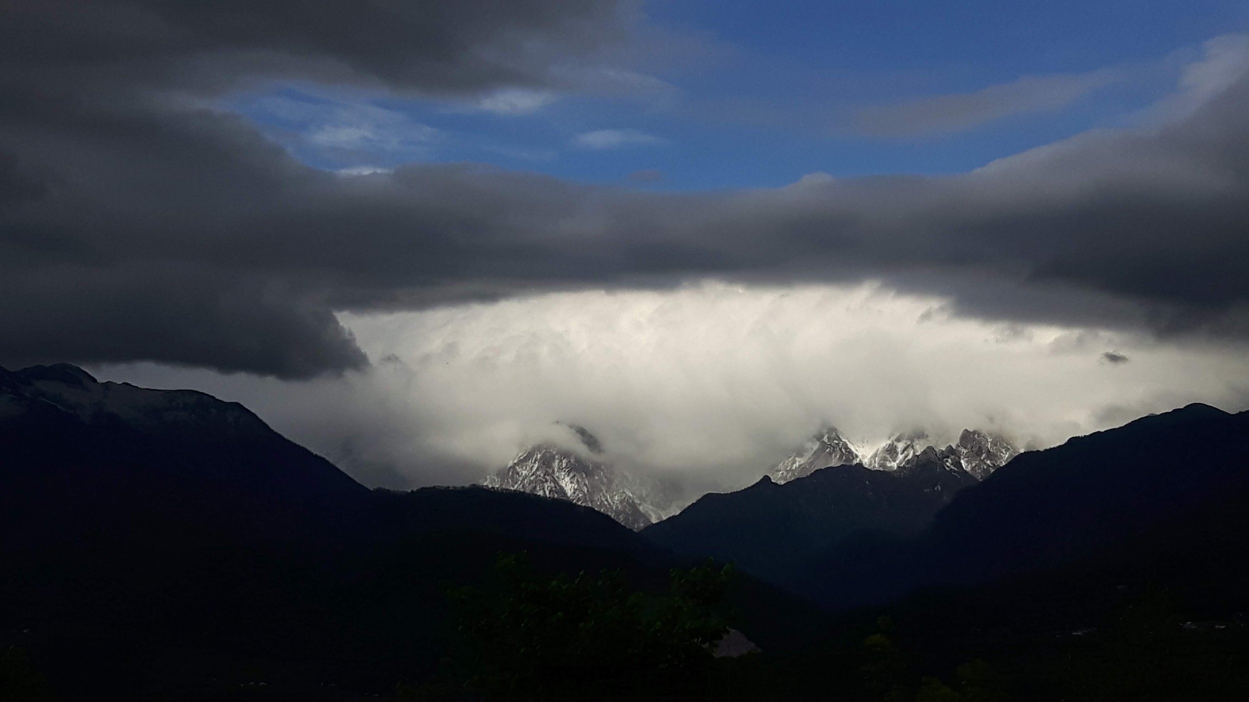 Dark clouds over snow-capped mountains with a mixture of blue sky and stormy weather.