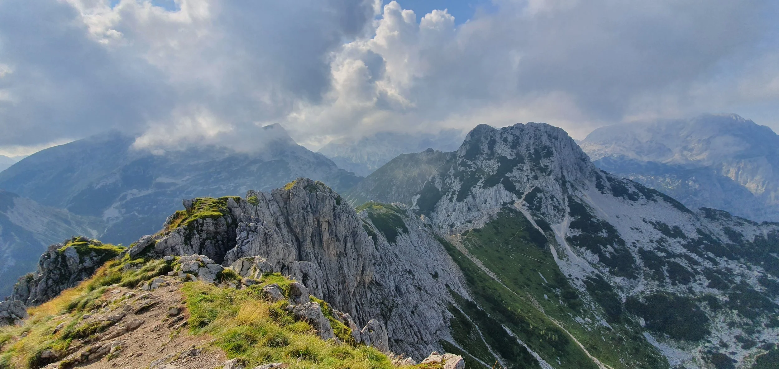 Mountains with green and rocky slopes under a partly cloudy sky.