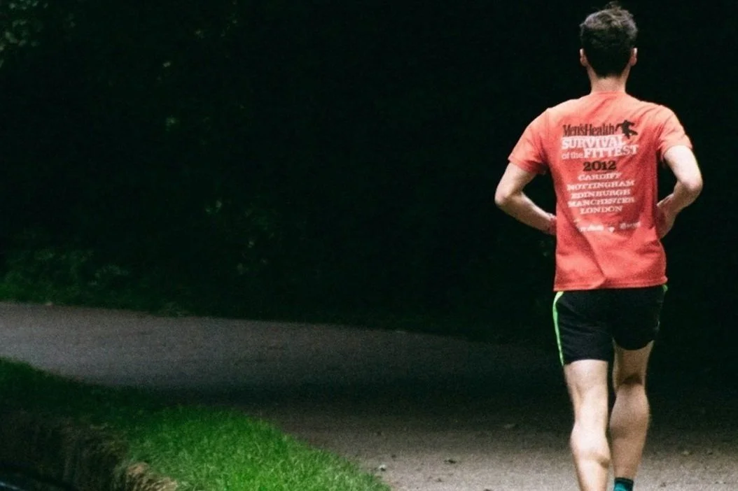 A person jogging on a dark outdoor path at night, wearing a red T-shirt and black shorts.