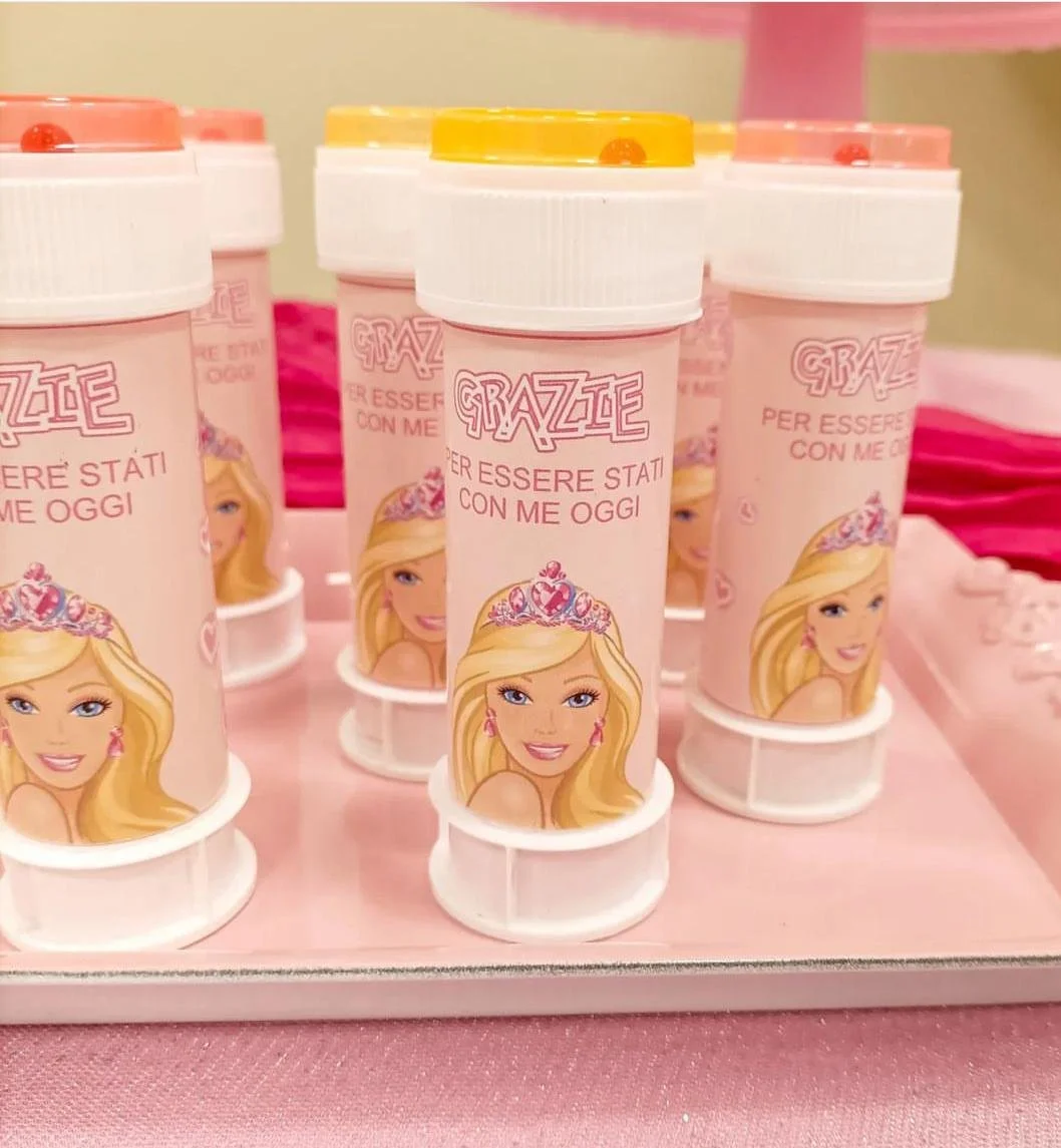 Contenitori rosa con etichetta con immagine di una principessa, decorati con coperchi gialli o rosa, posti su un vassoio rosa.