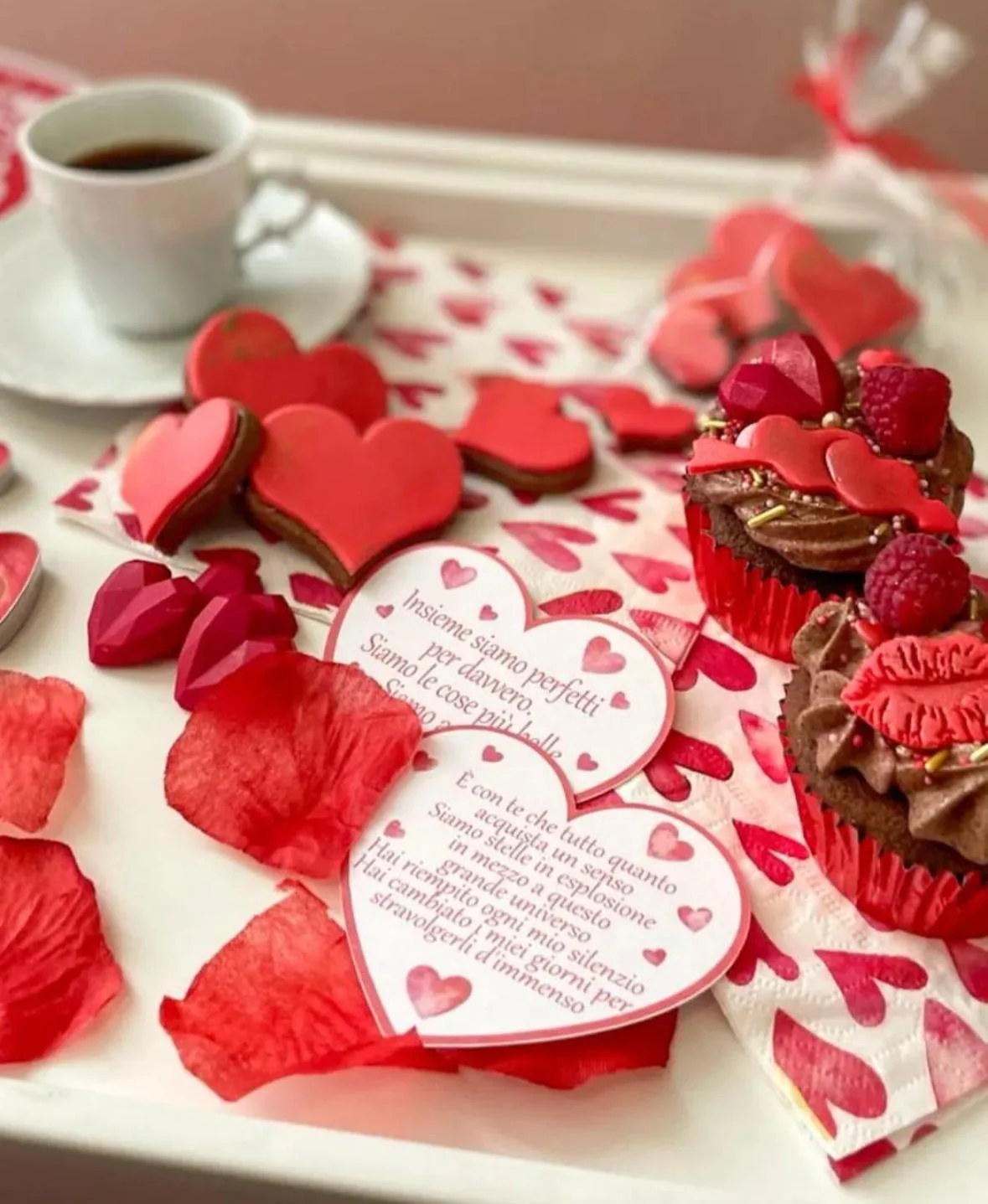 Cuore di cioccolato decorato con lamponi e caramelle, cupcakes con glassa al cioccolato e lamponi, tazza di caffè, petali di rosa e biglietti d'amore con messaggi romantici.