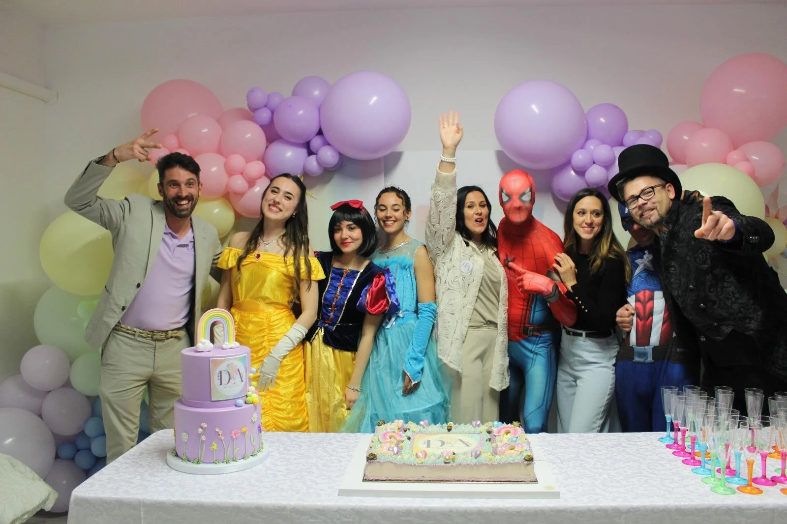 Gruppo di persone in costume di fantasia e supereroi, festeggiando con torta e decorazioni di palloncini color pastello