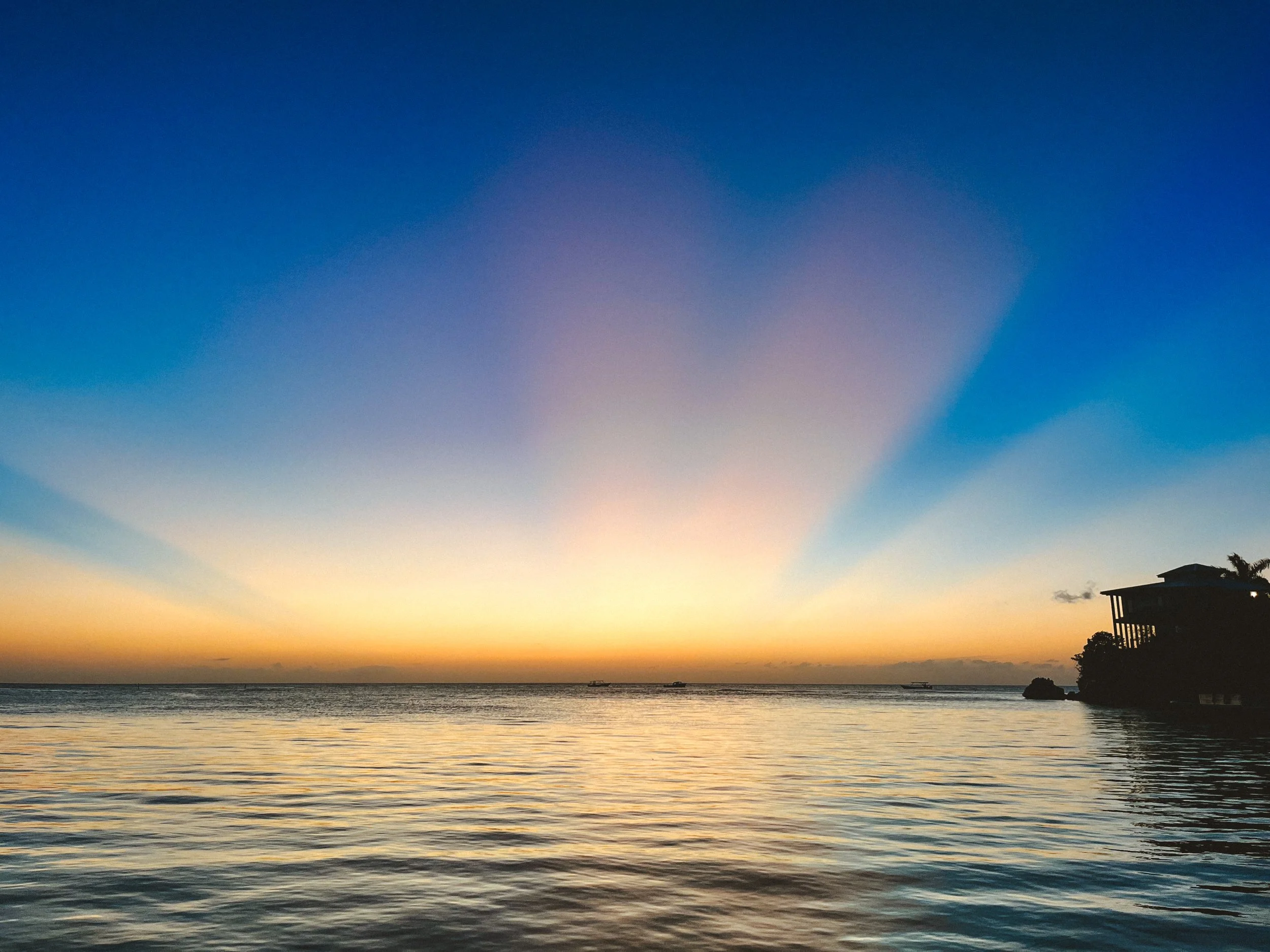 Sunset over the ocean with colorful sky and a silhouette of a building and palm tree on the right.