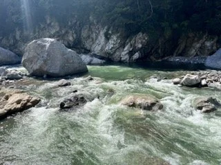 Flowing river with rocks and a large boulder in a natural outdoor setting.