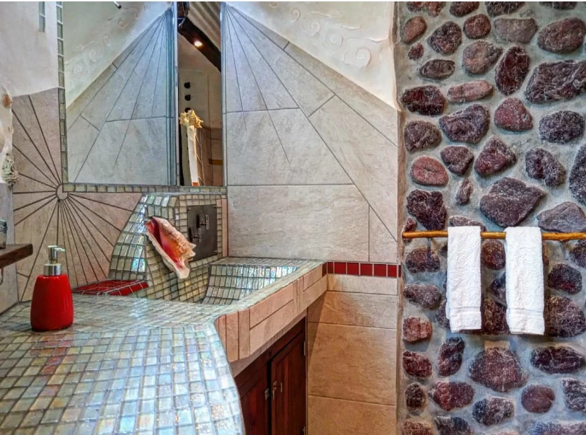Bathroom with mosaic and tiled surfaces, decorative mirror, soap dispenser, and a towel rack with two white towels