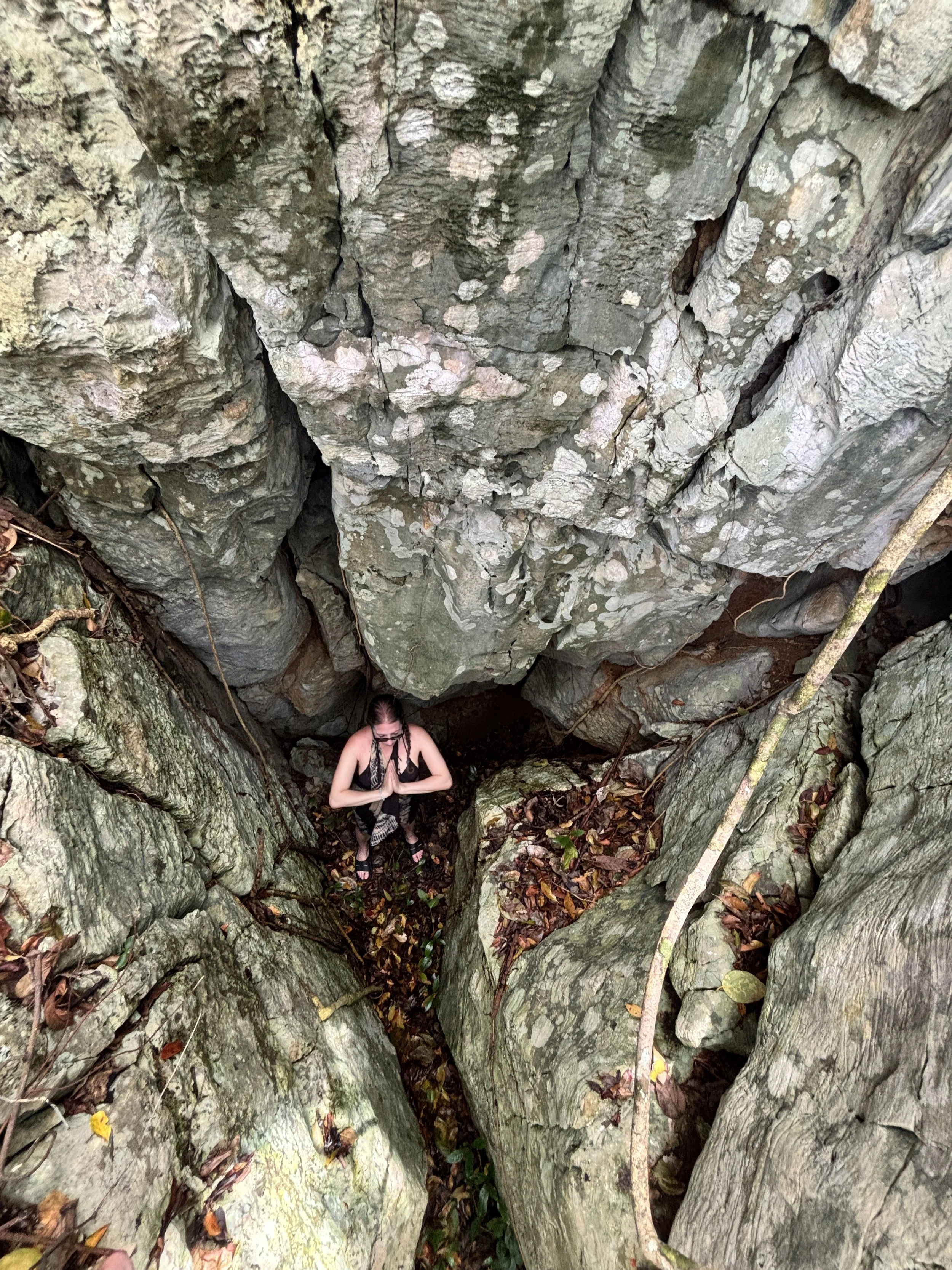 Person meditating in a small crevice between large rock formations surrounded by fallen leaves.