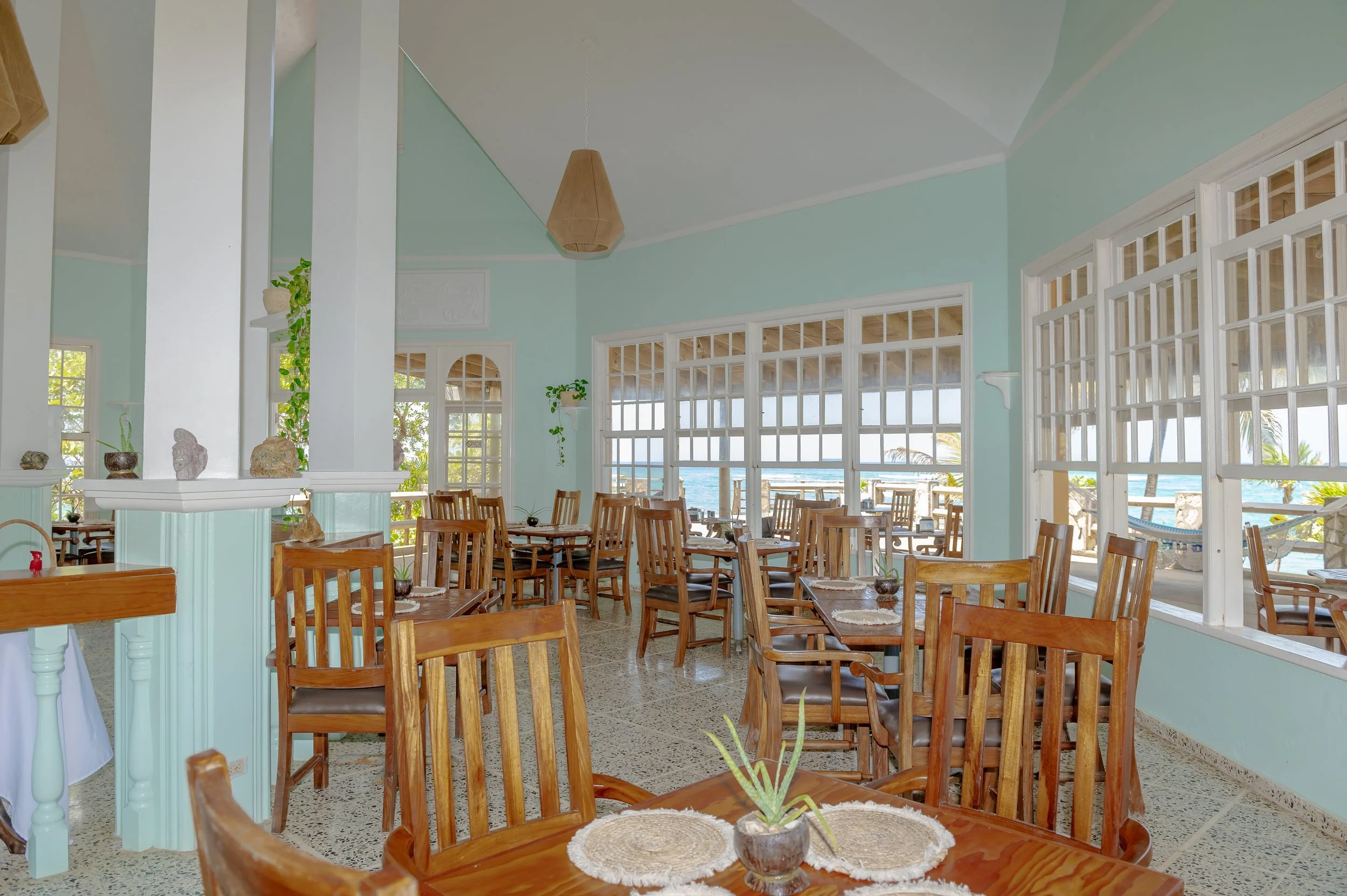 Beachside restaurant with wooden chairs, large windows, and ocean view in the background.