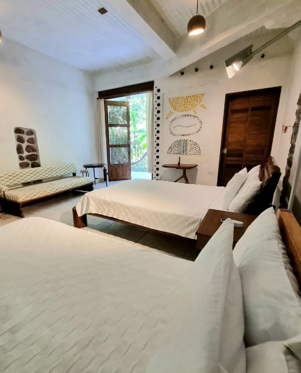A hotel room with two beds, a bench, a door leading outside, and artistic wall decorations.