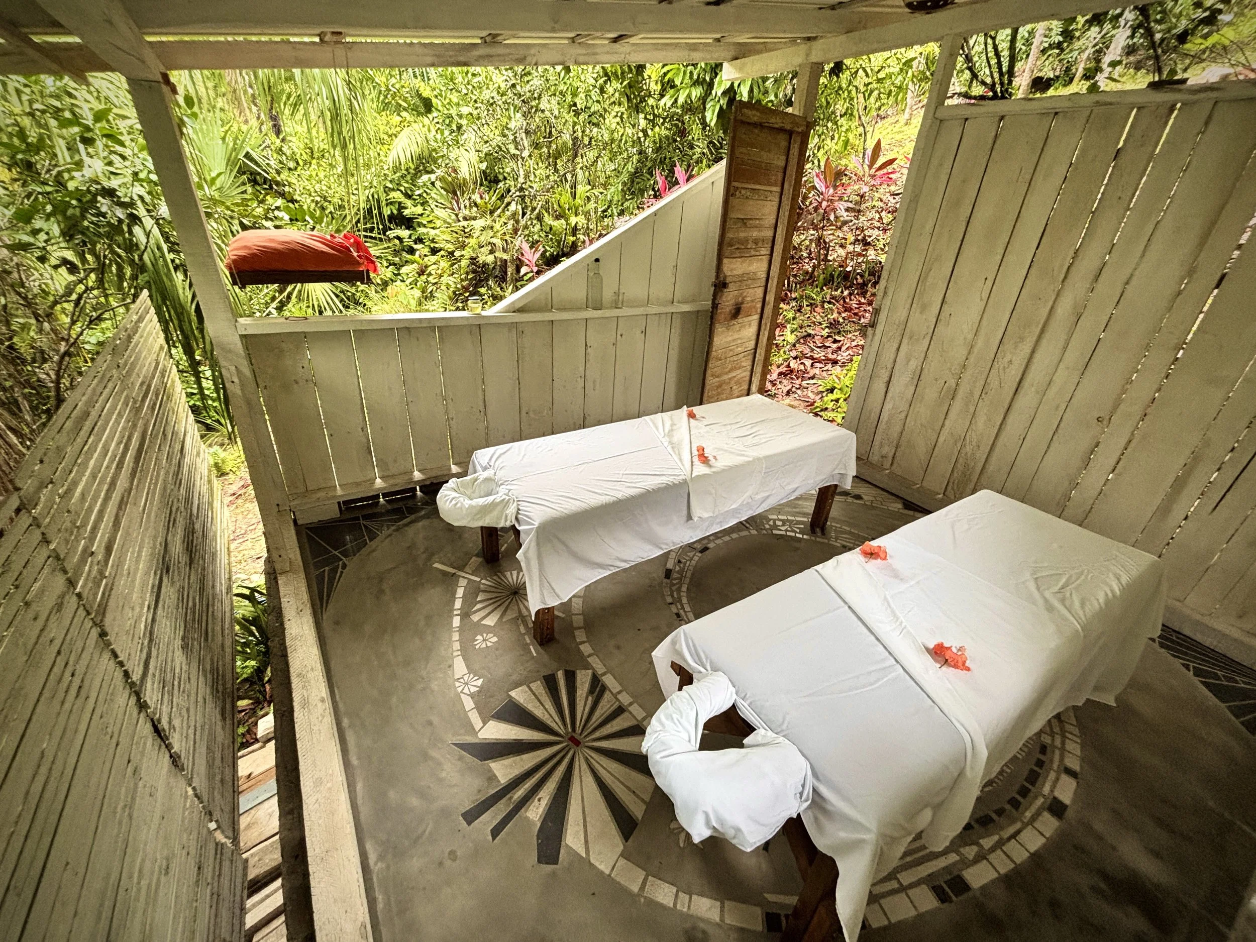 Two massage tables with white linens and flower petals in a bamboo hut surrounded by lush jungle at Omega Lodge, Honduras