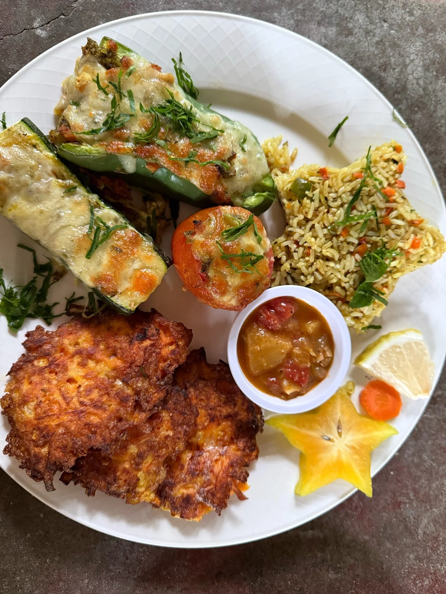 A plate of Indian cuisine including stuffed vegetables, rice, fried chicken, a lemon wedge, a starfruit slice, a small bowl of curry, and vegetable garnishes.