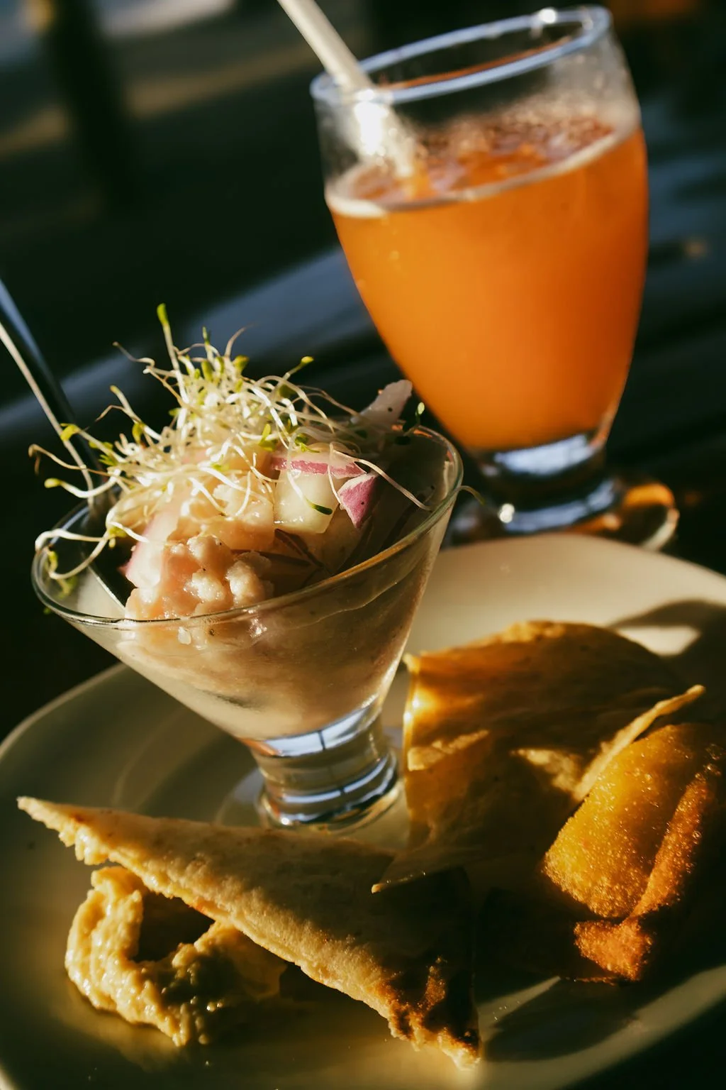 A glass of orange juice, a small bowl of ceviche garnished with sprouts, and a plate with fried plantains and a tortilla chip.