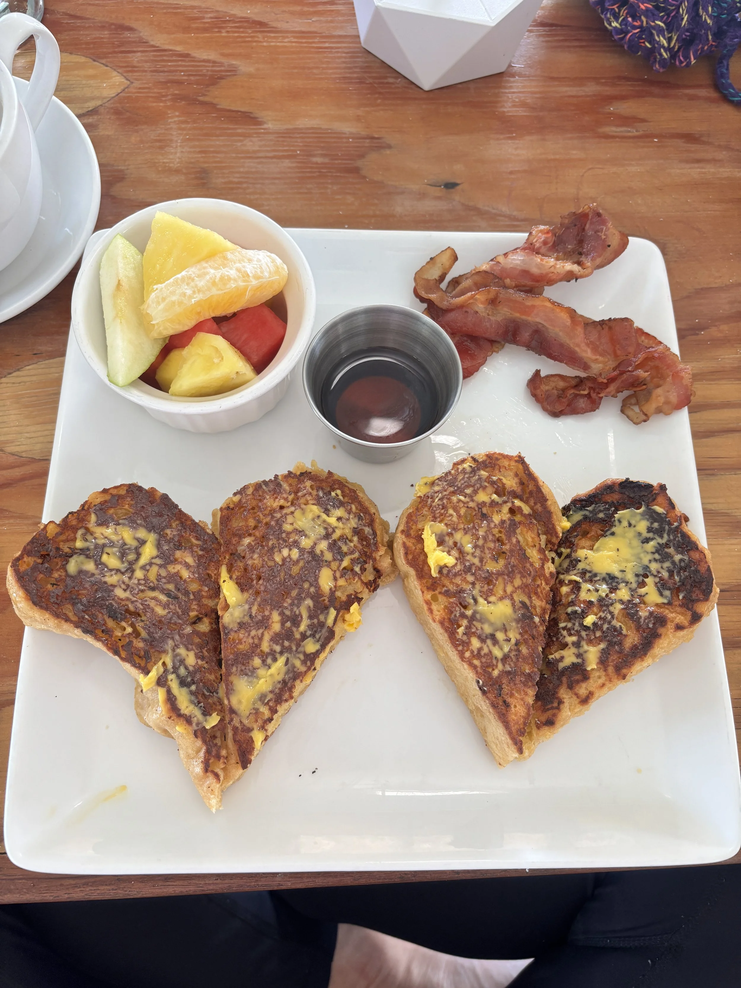 French toast with butter, bacon, fresh fruit salad, and syrup on a white plate.