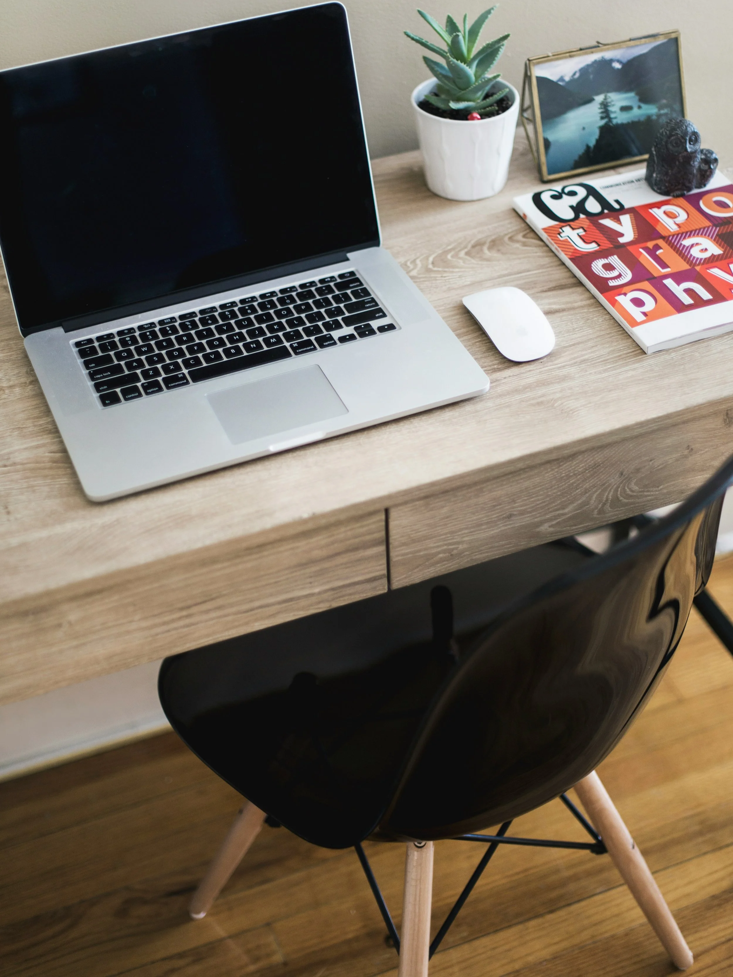 Desk with a laptop, wireless mouse, potted succulent, various framed photos and artwork, and a book.