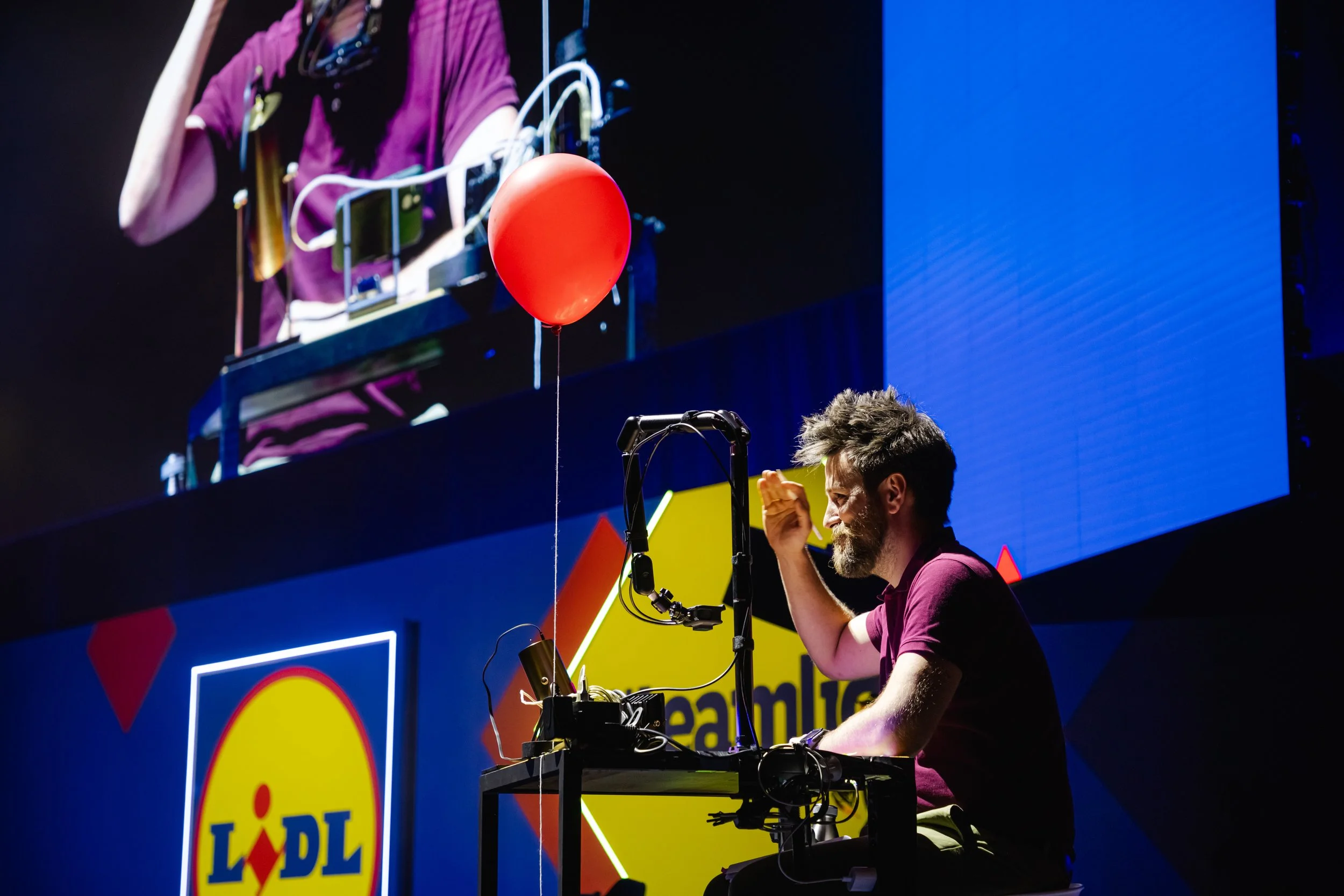 Grillo Visual Thinking para Lidl, dibujando en un live graphic recording en una tableta, en una mesa y un globo rojo, mientras una pantalla grande muestra una imagen de él en el escenario. Logo de Lidl visible en el fondo.