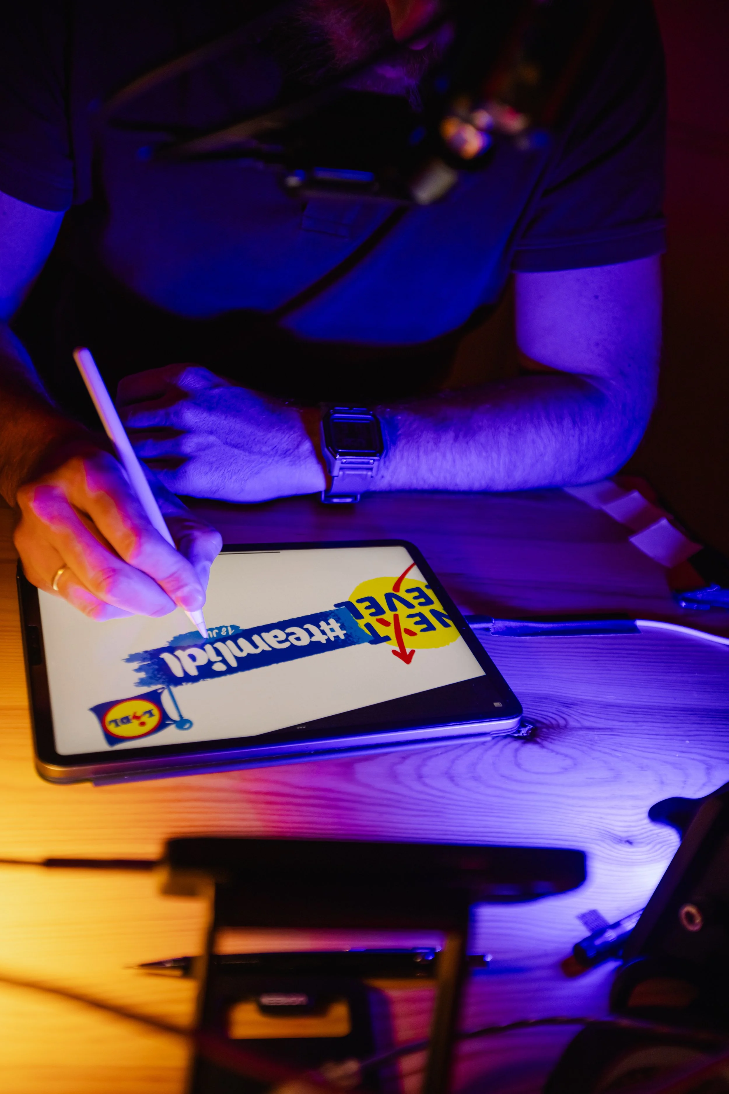 Grillo Visual Thinking para Lidl, dibujando en un live graphic recording en una tableta en evento llamado #temalidl y en un entorno con iluminación colorida, rodeada de dispositivos electrónicos y accesorios en una mesa de madera.