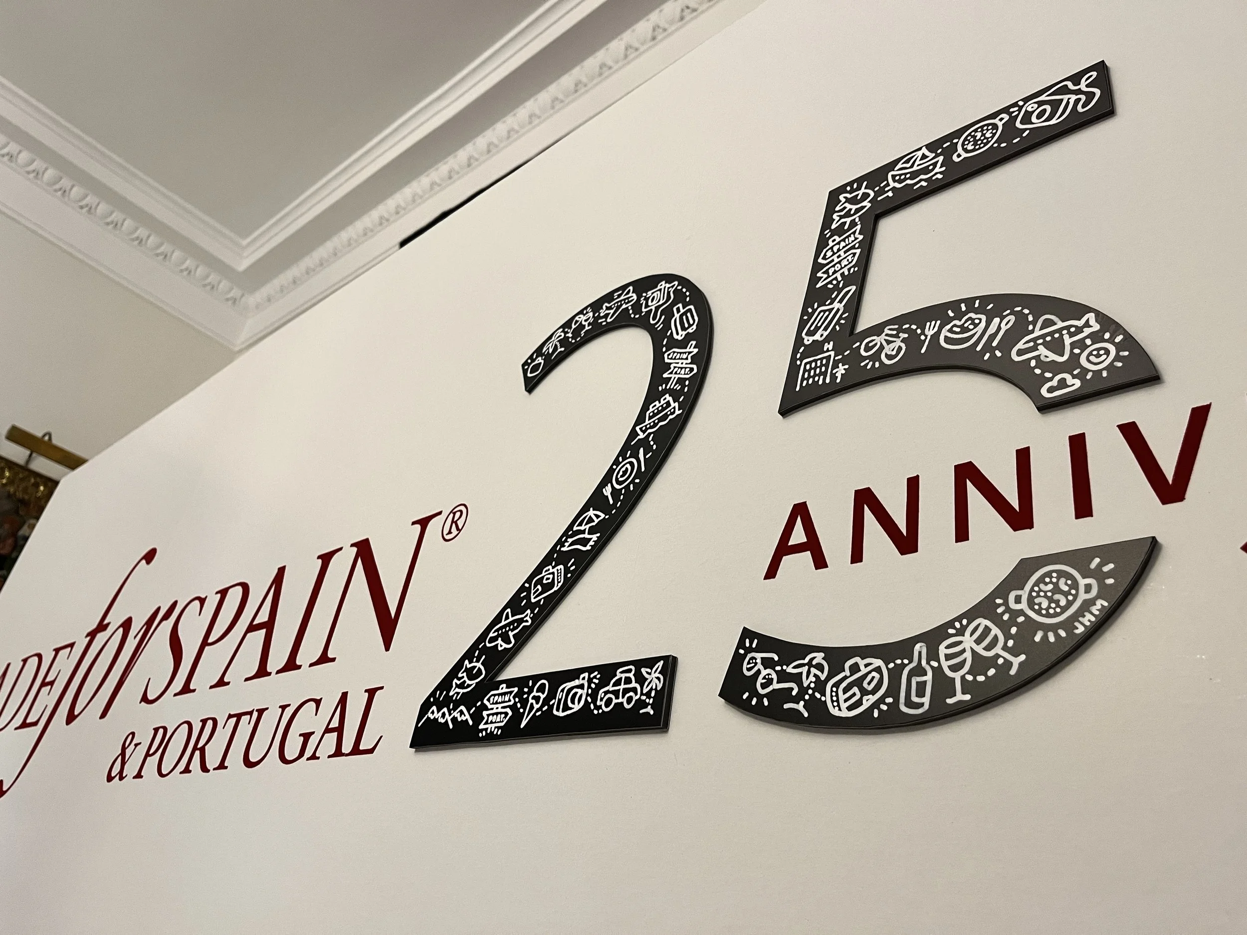 Decorativo letrero con el número 25, rodeado de iconos relacionados con viajes y cultura, en celebración del 25 aniversario de una organización, con palabras en español que dicen 'Aniversario de Made For Spain & Portugal'.