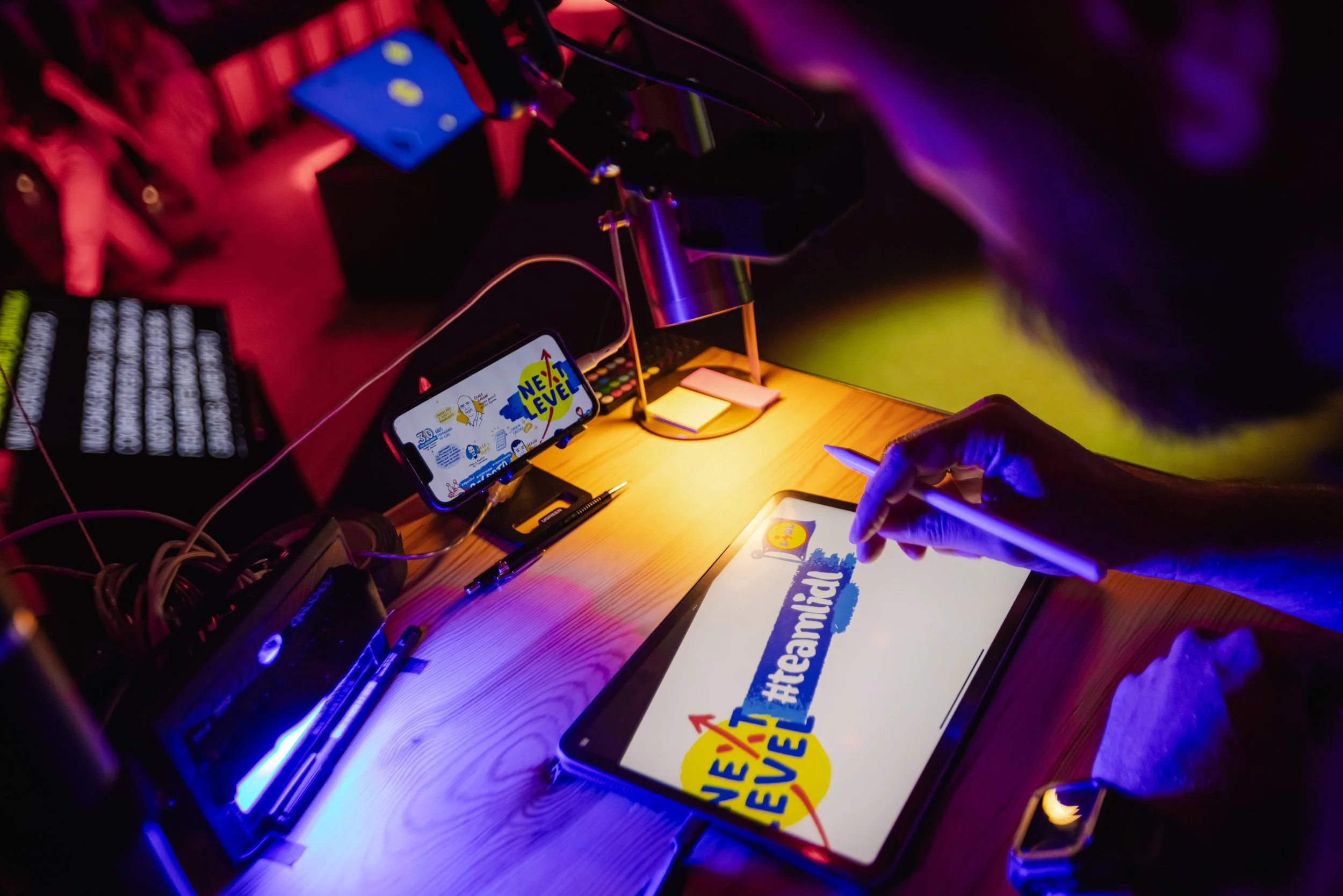 Grillo Visual Thinking para Lidl, dibujando en un live graphic recording en una tableta con el hashtag #teamIidl en un entorno con luces de colores y otros dispositivos electrónicos en una mesa de madera.