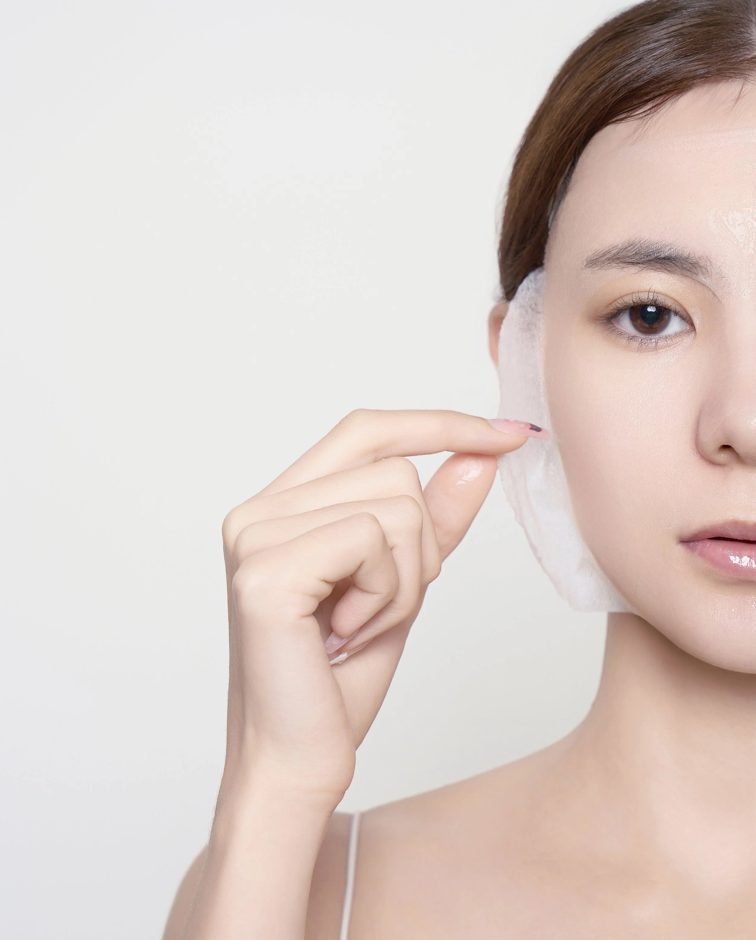 A woman with light skin and brown hair holding a cotton pad to her face, emphasizing skincare or makeup removal.