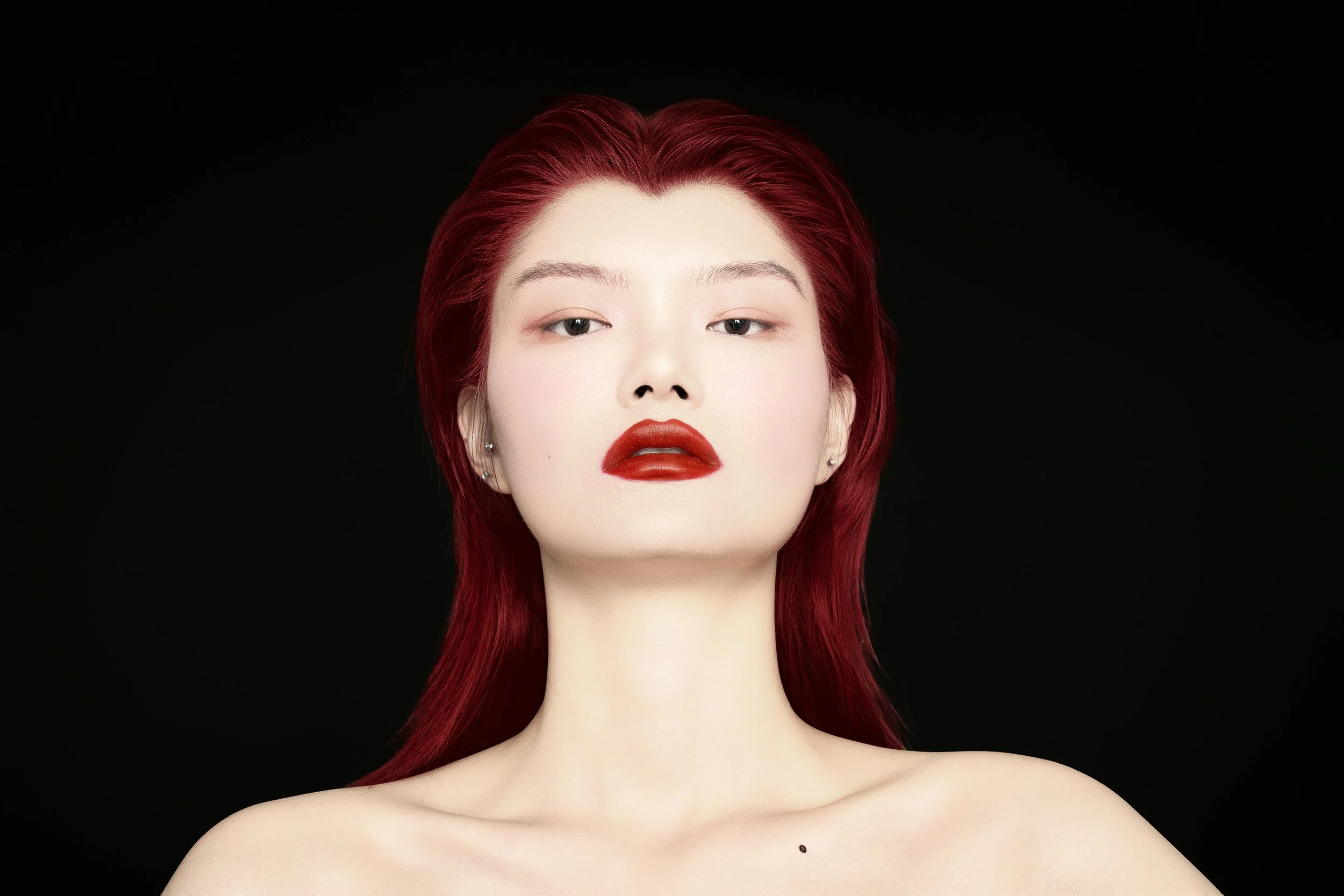 A woman with red hair and bold red lipstick against a black background.