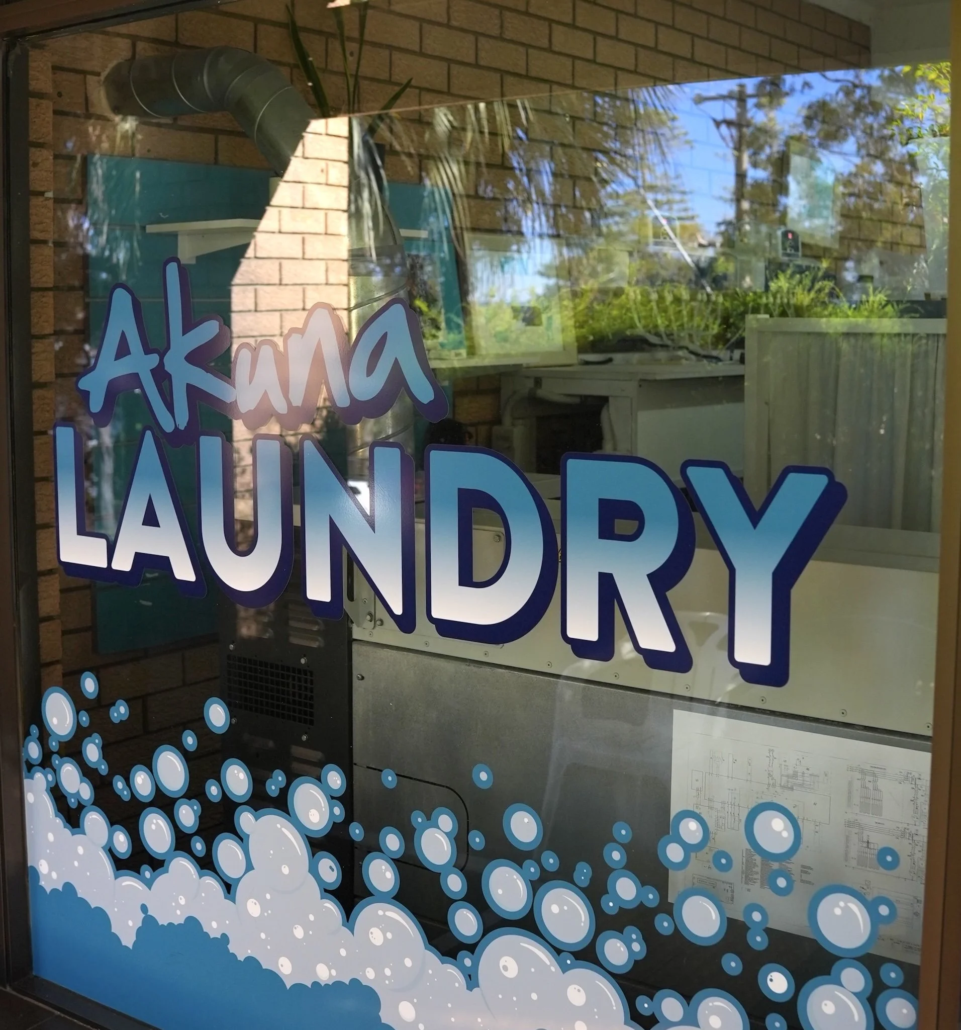 Sign on a window reading 'Akuna Laundry' with blue bubbles at the bottom.
