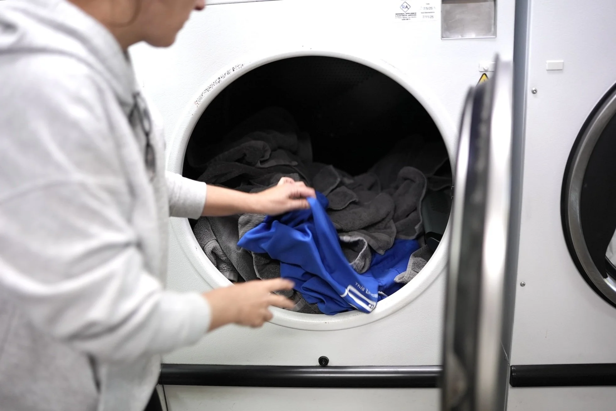 Person loading colorful laundry into a front-loading washing machine in a laundromat.