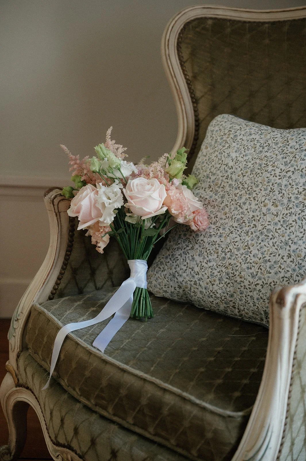 Een bloemstuk met roze en witte bloemen ligt op een vintage bank met een sierlijk houten frame en een kussensloop met een bloemenpatroon.