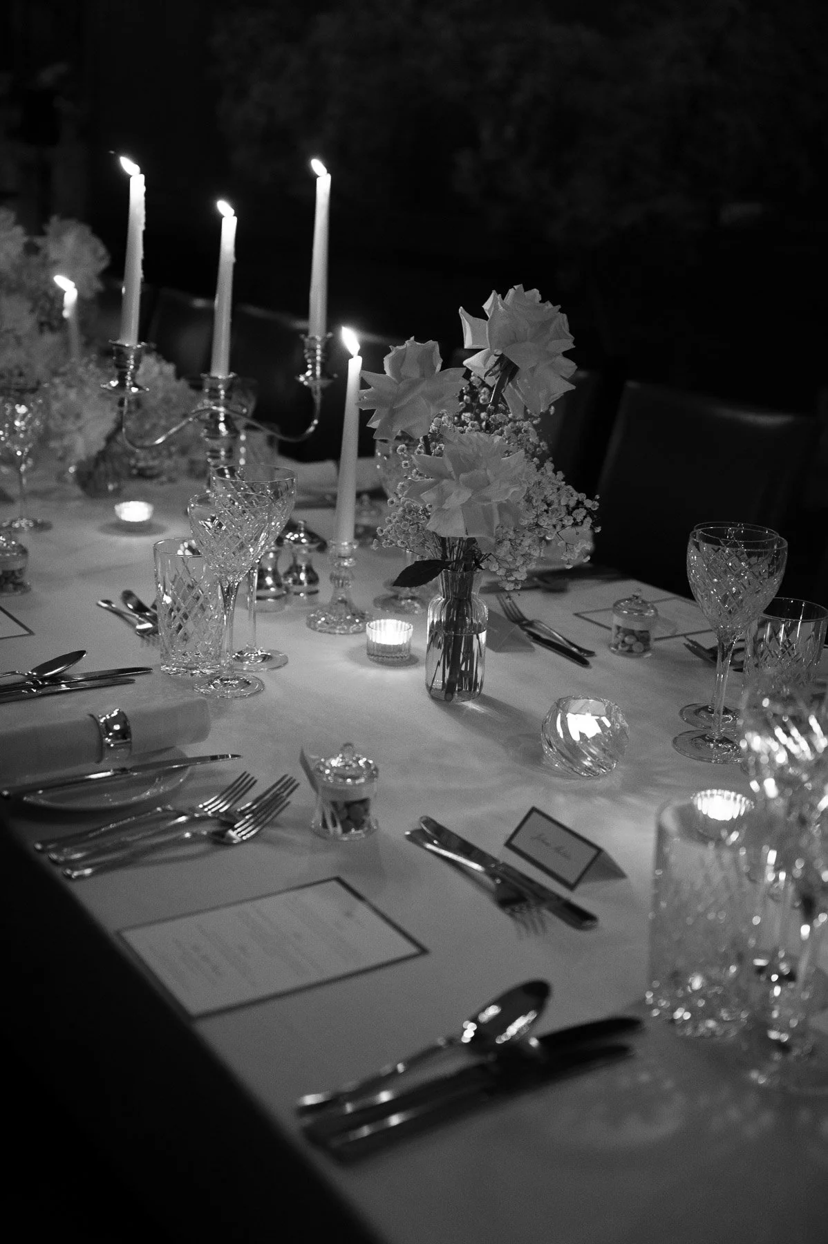 Een elegante tafelsetting met kaarsen, glaswerk, bloemen en menu's, klaar voor een diner.