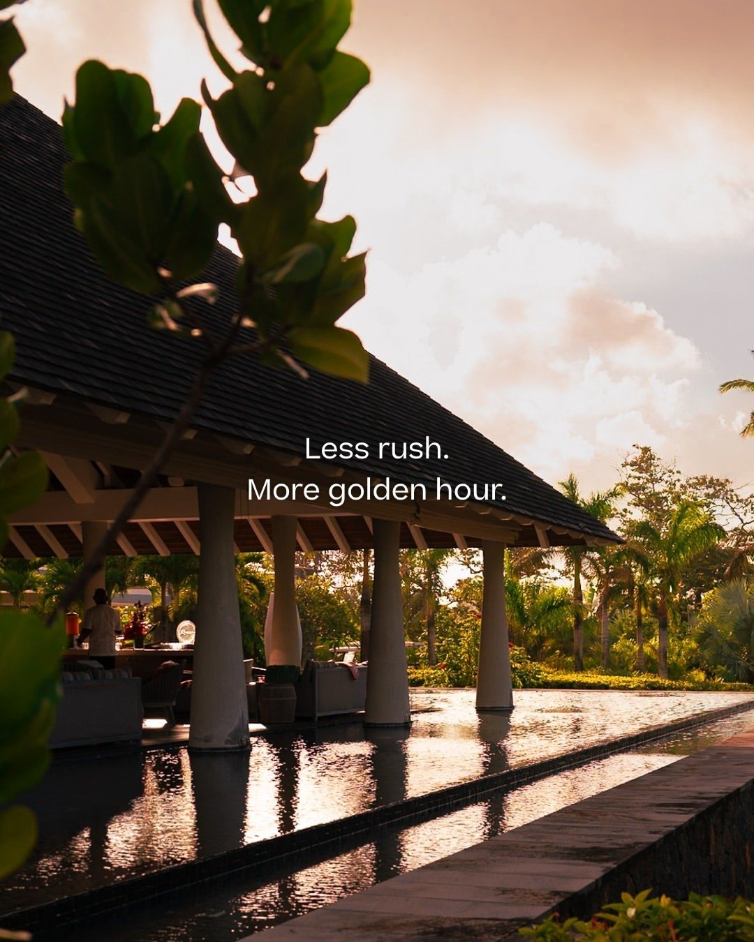 A tropical resort setting at sunset with a thatched-roof pavilion, green trees, and a reflecting pool, with the text 'Less rush. More golden hour.'