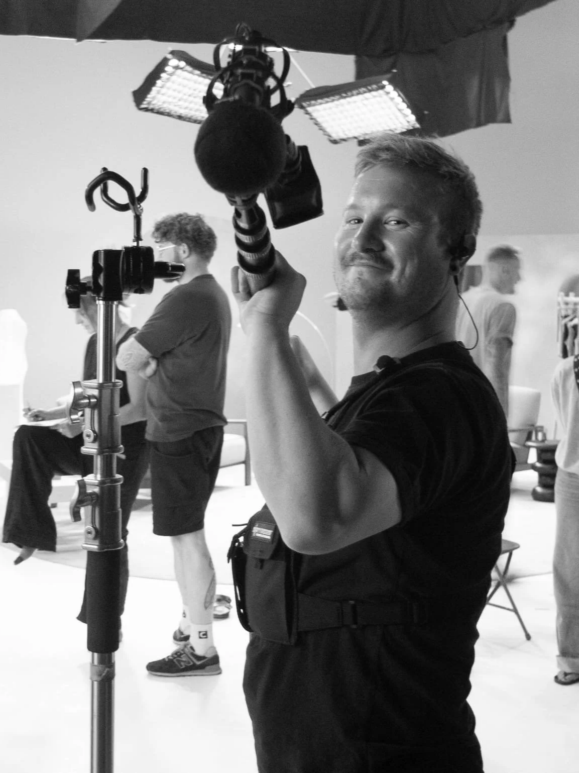 Sound recordist holding a boom microphone on a commercial fashion shoot in London, with crew and models in the background
