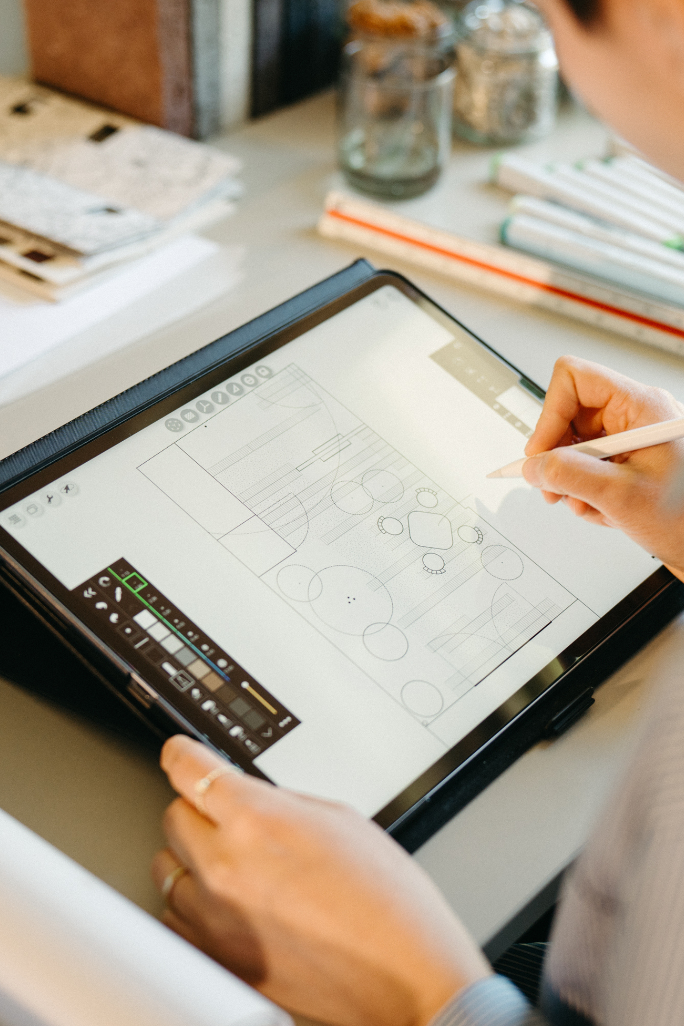 Een vrouw van Studio Jong Baw schetst een tuinontwerp voor een ecologische stadstuin, en gebruikt daarbij kleurstalen van Farrow & Ball, een boek over planten en materialen ter inspiratie