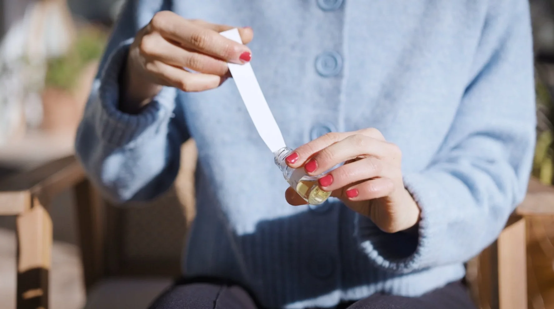 Une personne met une pipette dans une petite bouteille contenant un liquide jaune clair, en extérieur.