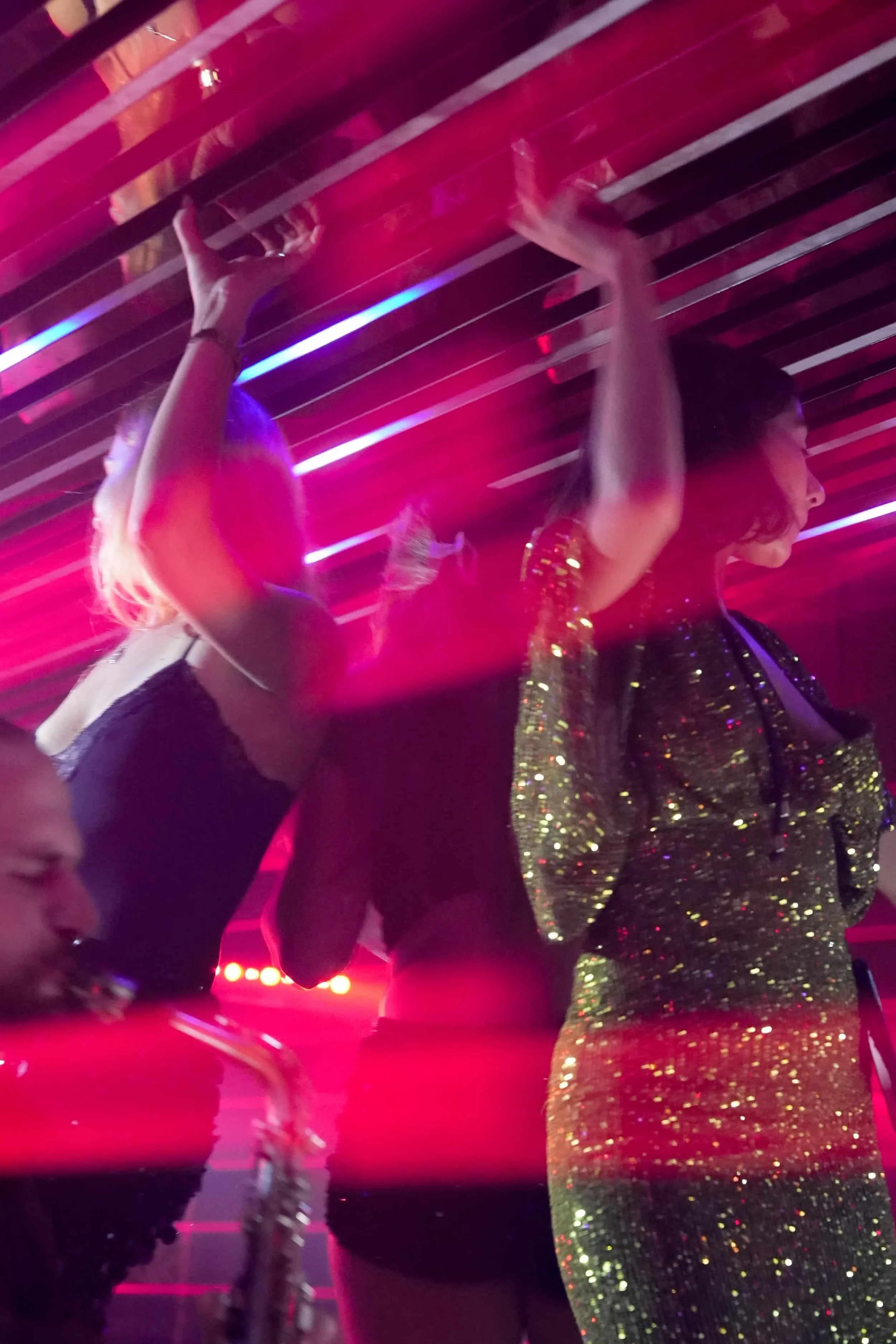 Deux femmes dansent et semblent profiter de la fête, une joue du saxophone, dans un environnement éclairé par des lumières de couleur rouge et violette.