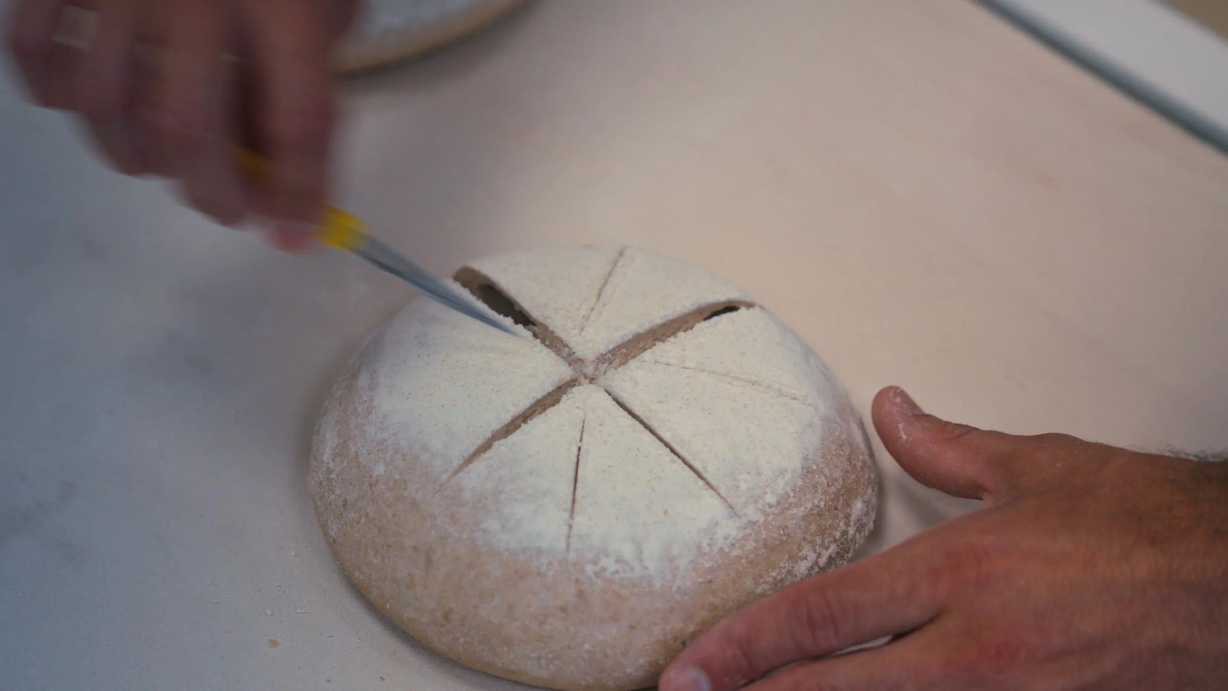 Une personne coupe un gâteau rond, recouvert de sucre glace, en sept parts égales à l'aide d'un couteau. La main de l'autre personne est visible, posée sur la surface où repose le gâteau.