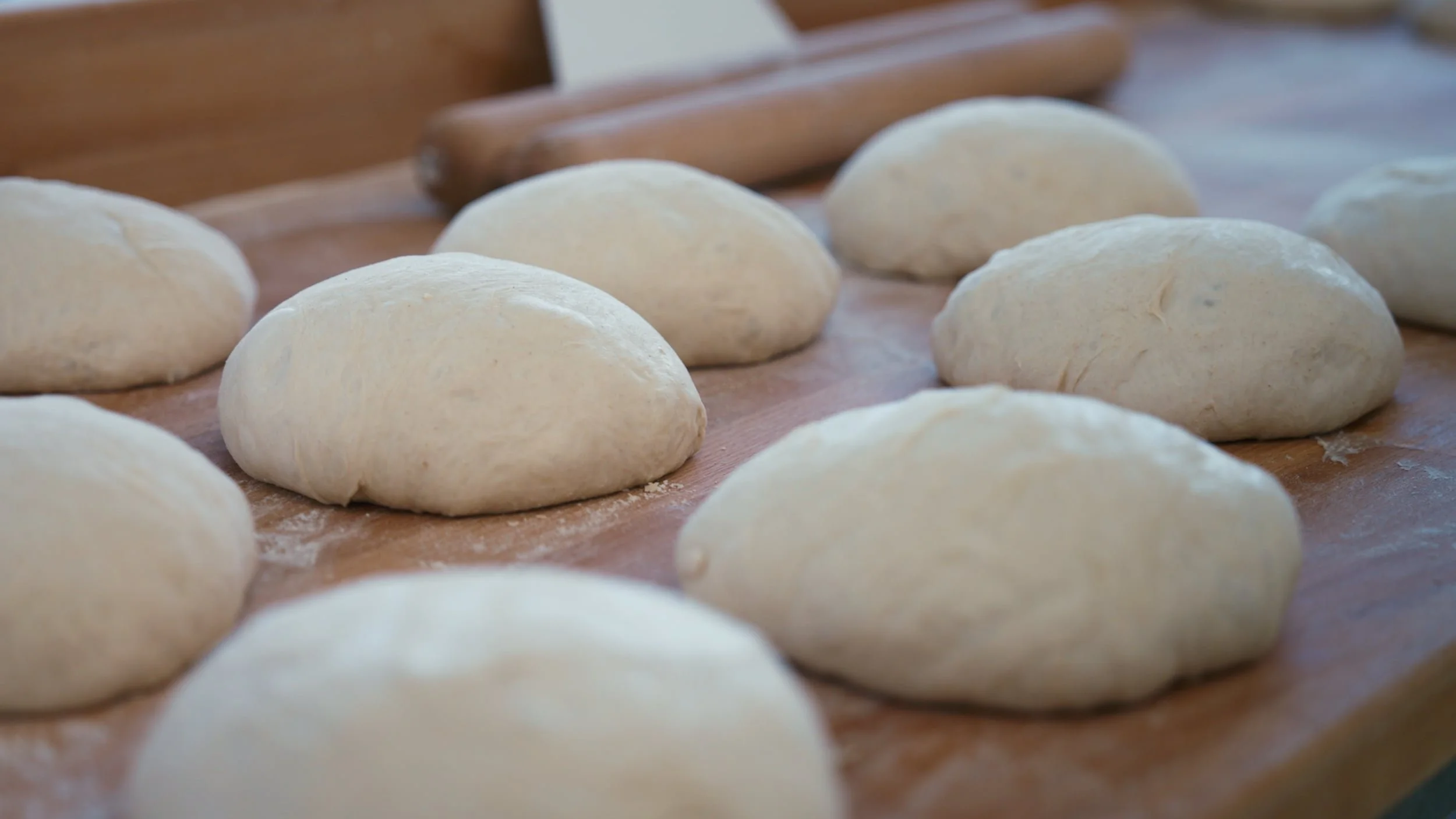 Des boules de pâte à pain sur un plan de travail en bois, prêtes à être façonnées.