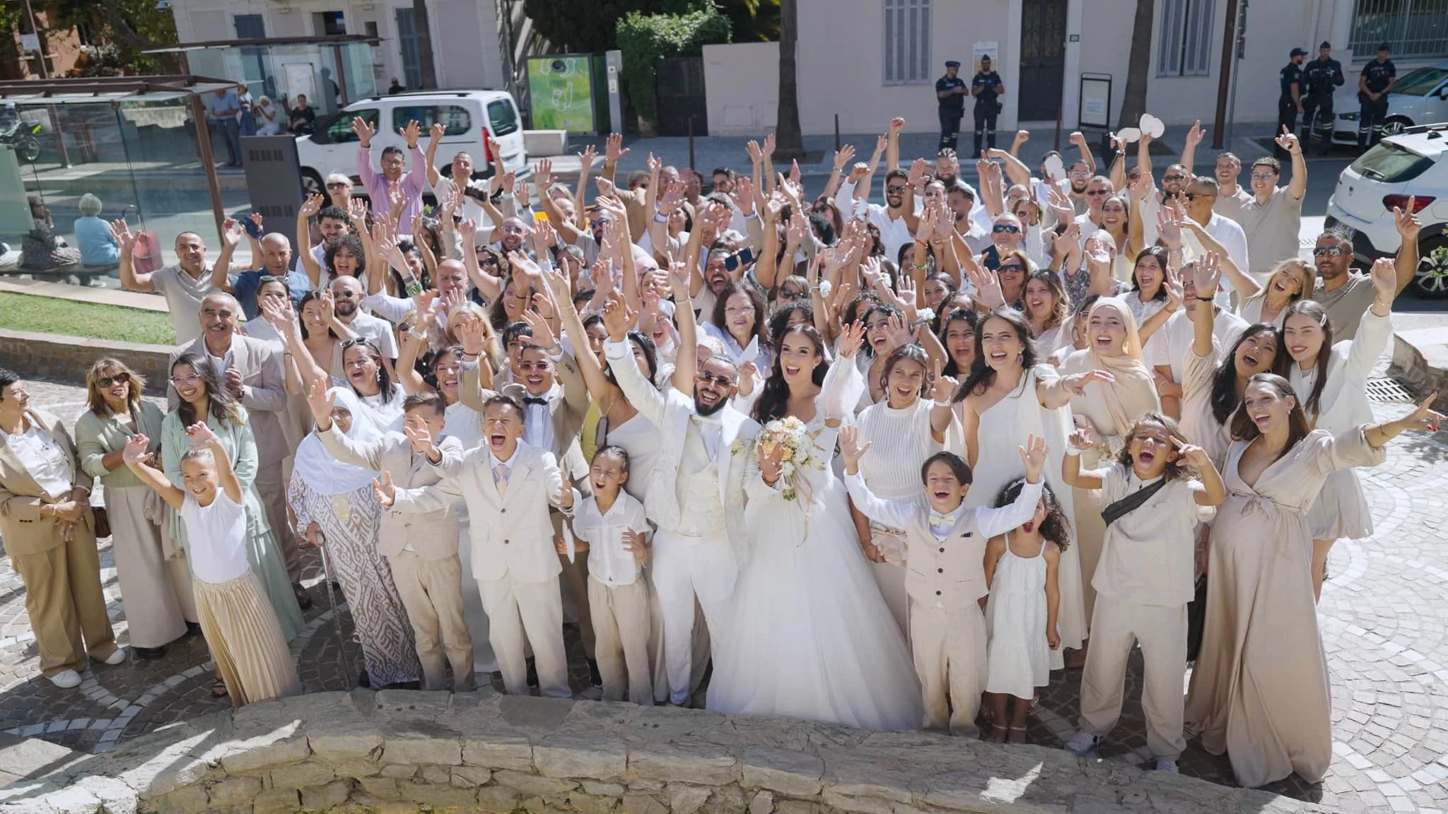 Groupe de personnes lors d'un mariage, souriantes et levant les bras, avec le couple de mariés au centre.