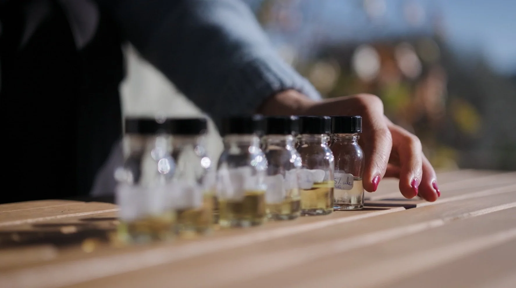 Main tenant des petits bocaux avec liquide sur une table en bois.