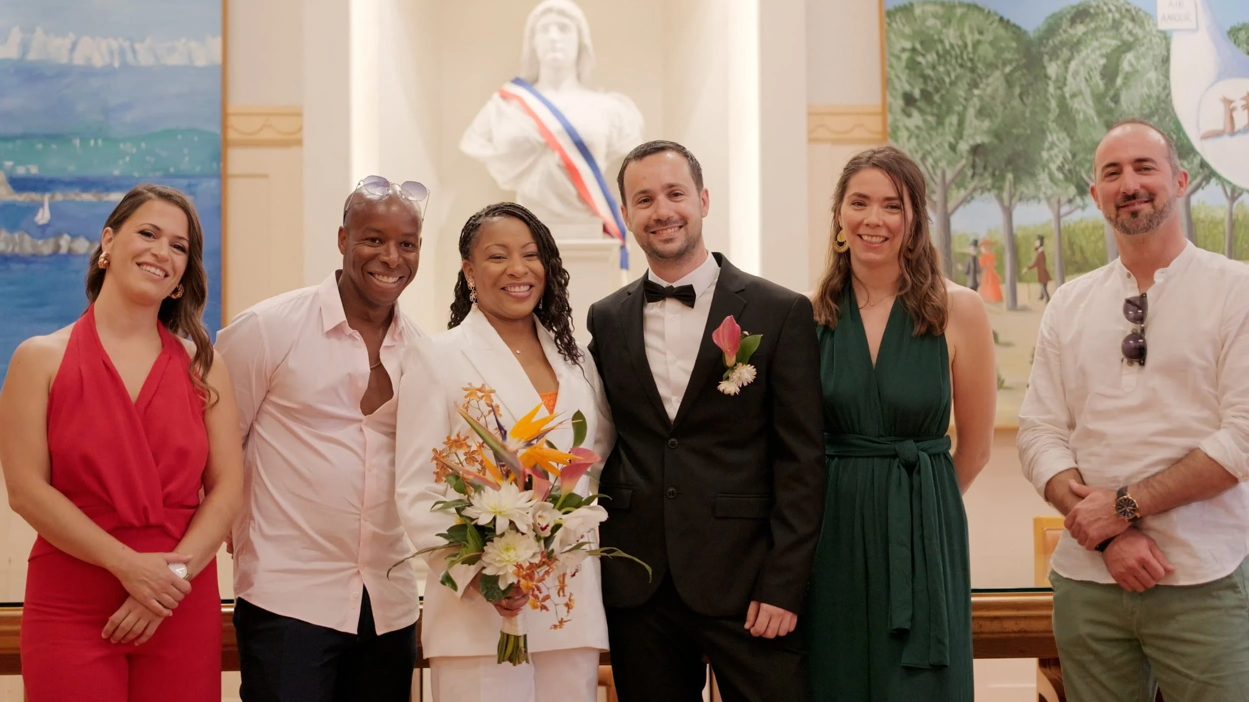 Un groupe de sept personnes posant pour une photo lors d'une cérémonie ou d’un événement formel dans une salle décorée avec des peintures et une statue.
