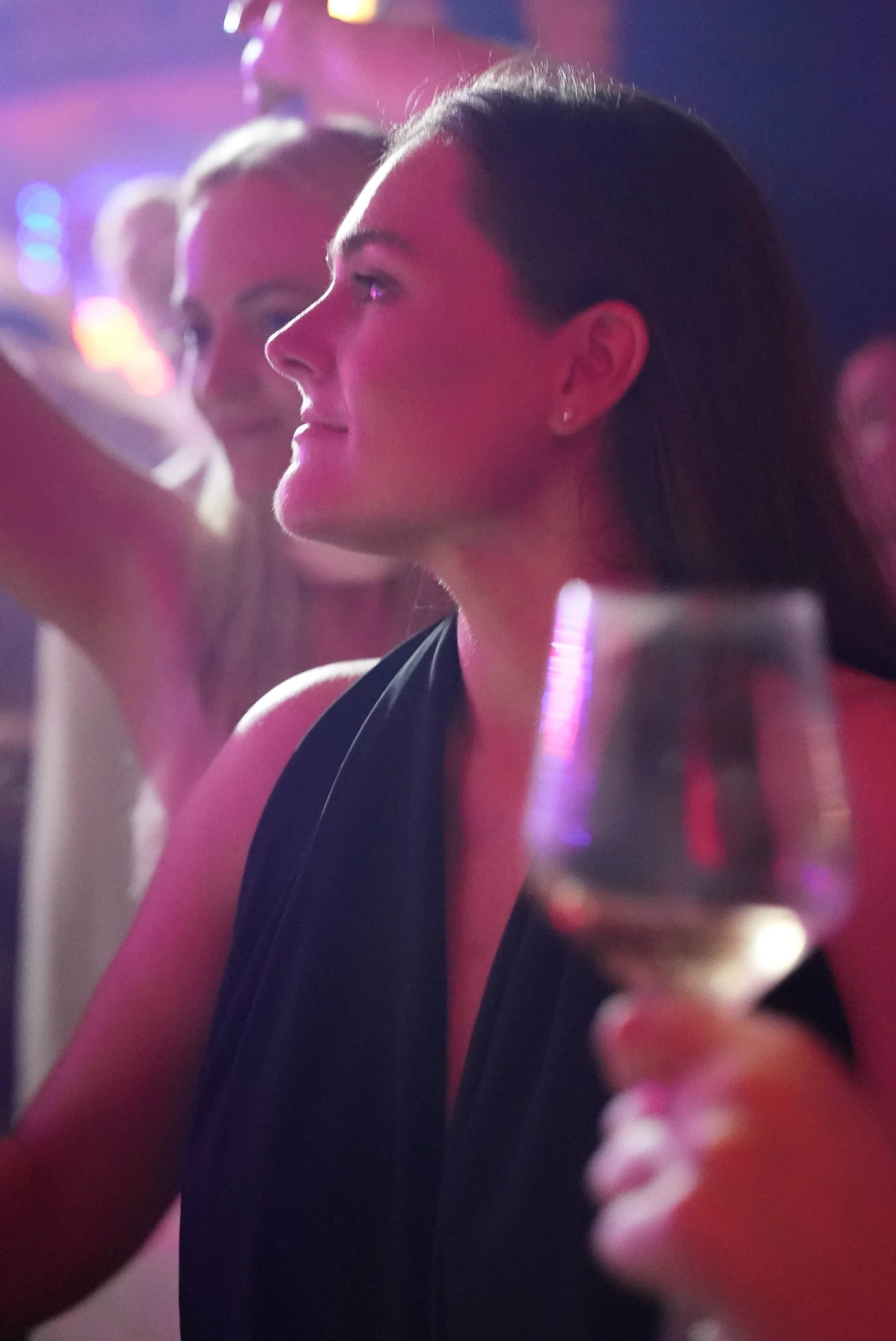 Deux femmes dans une ambiance lumineuse et festive, l'une souriante et regardant vers laquelle on ne voit pas, tenant un verre de vin blanc.