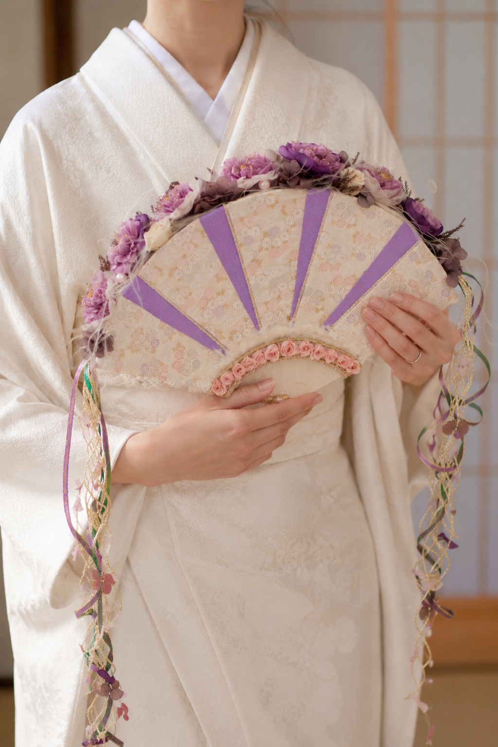 MASAKO MODESTEが15年以上にわたり毎年開催してきたブーケショーで培ったデザインをもとに制作した、白無垢や白い和装に映える扇型のプリザーブドフラワーブーケ。紫やピンクの花々、繊細なリボン、上品な扇のデザインが、和装前撮りや結婚式本番に華やかさを添えます。プリザーブドフラワーをふんだんに使用しているため、前撮りから式本番まで同じブーケを使うことができ、挙式後は別の作品へ作り変えて一生の記念として飾っていただけます。