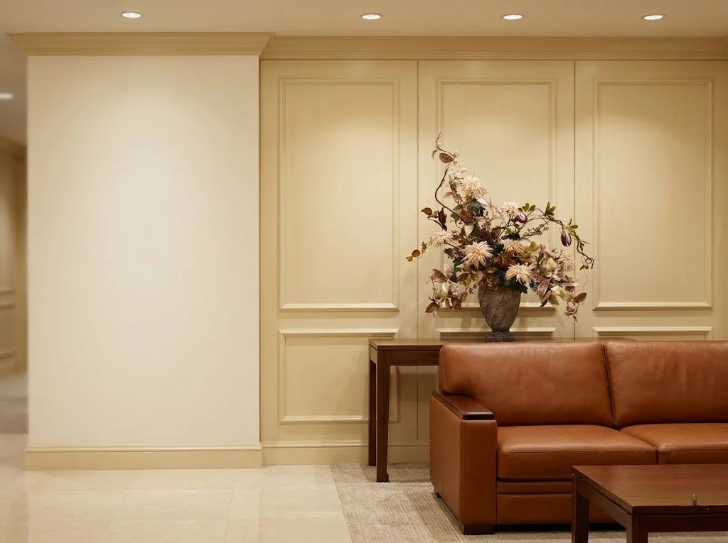 名古屋の法人向けレンタルフラワー（Masako Modeste）。高級感あふれる会議室のソファ横に飾られた、秋色を帯びた高品質なアーティフィシャルフラワー（造花）。デザイナー高松雅子による、石造りの花器と調和した洗練された作品が、ビジネス空間に格式高い癒しを提供します。