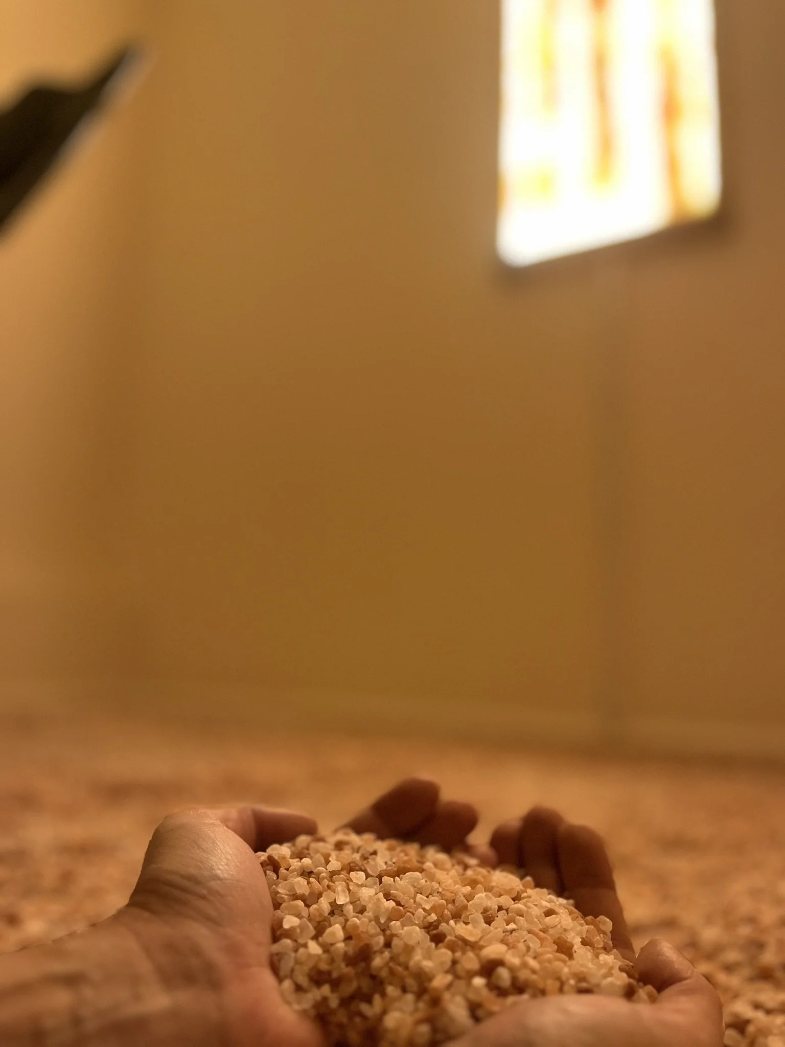 Close-up of a hand holding a handful of Himalayan salt crystals, with a Himalayan salt tile frame in the background.