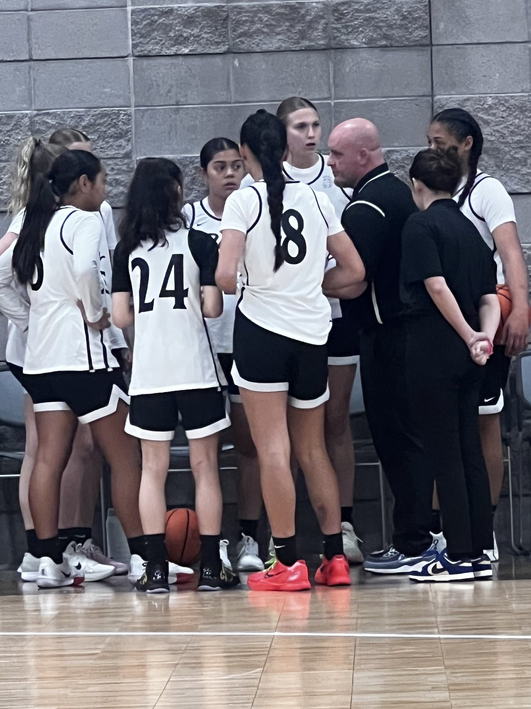 A women's volleyball team huddling with coach during a timeout.