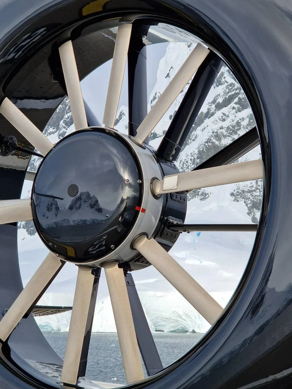 Close-up view of a telescope's mirror and support structure in a snowy, mountainous landscape.