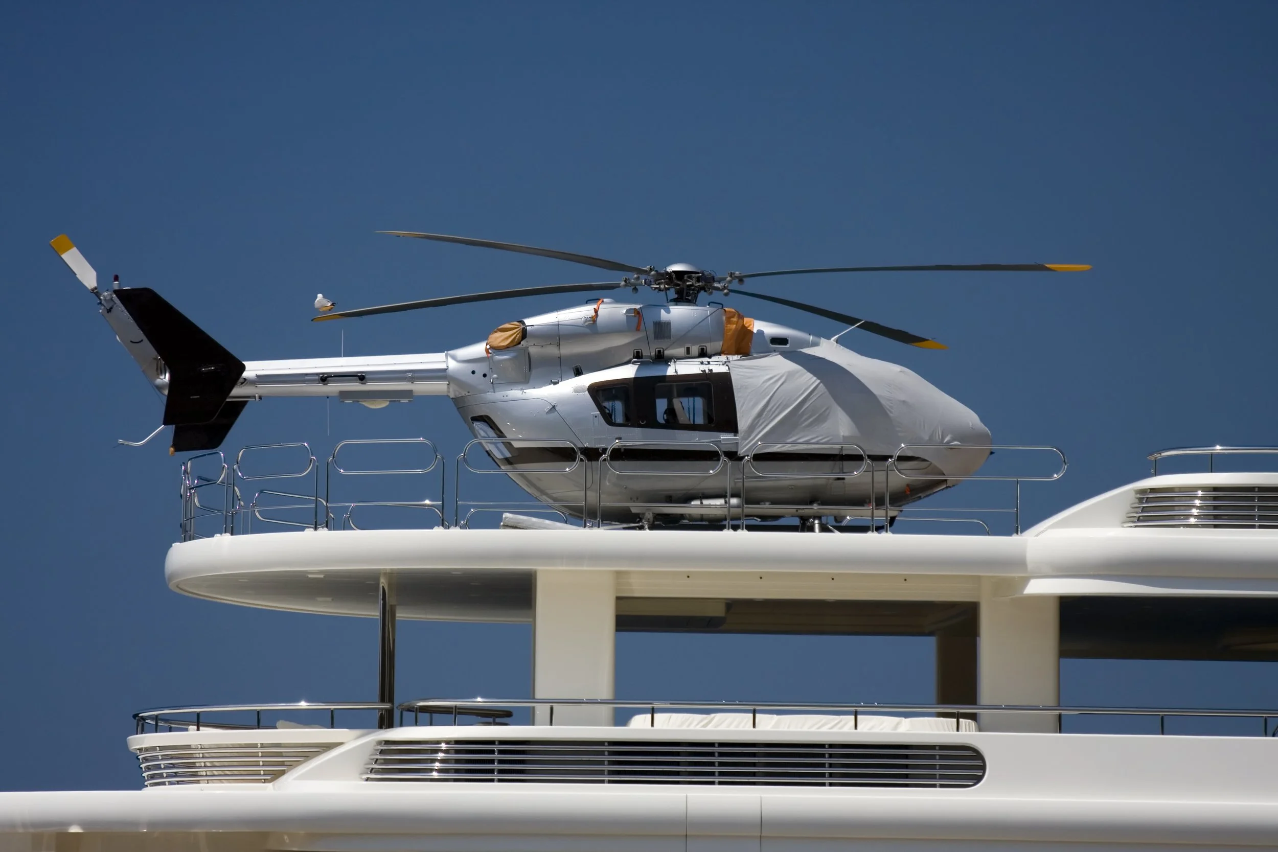A helicopter parked on the top deck of a yacht with a clear blue sky background.