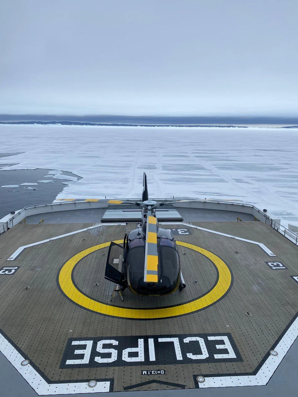 An aerial view of a helicopter on a helipad on a ship in icy waters.