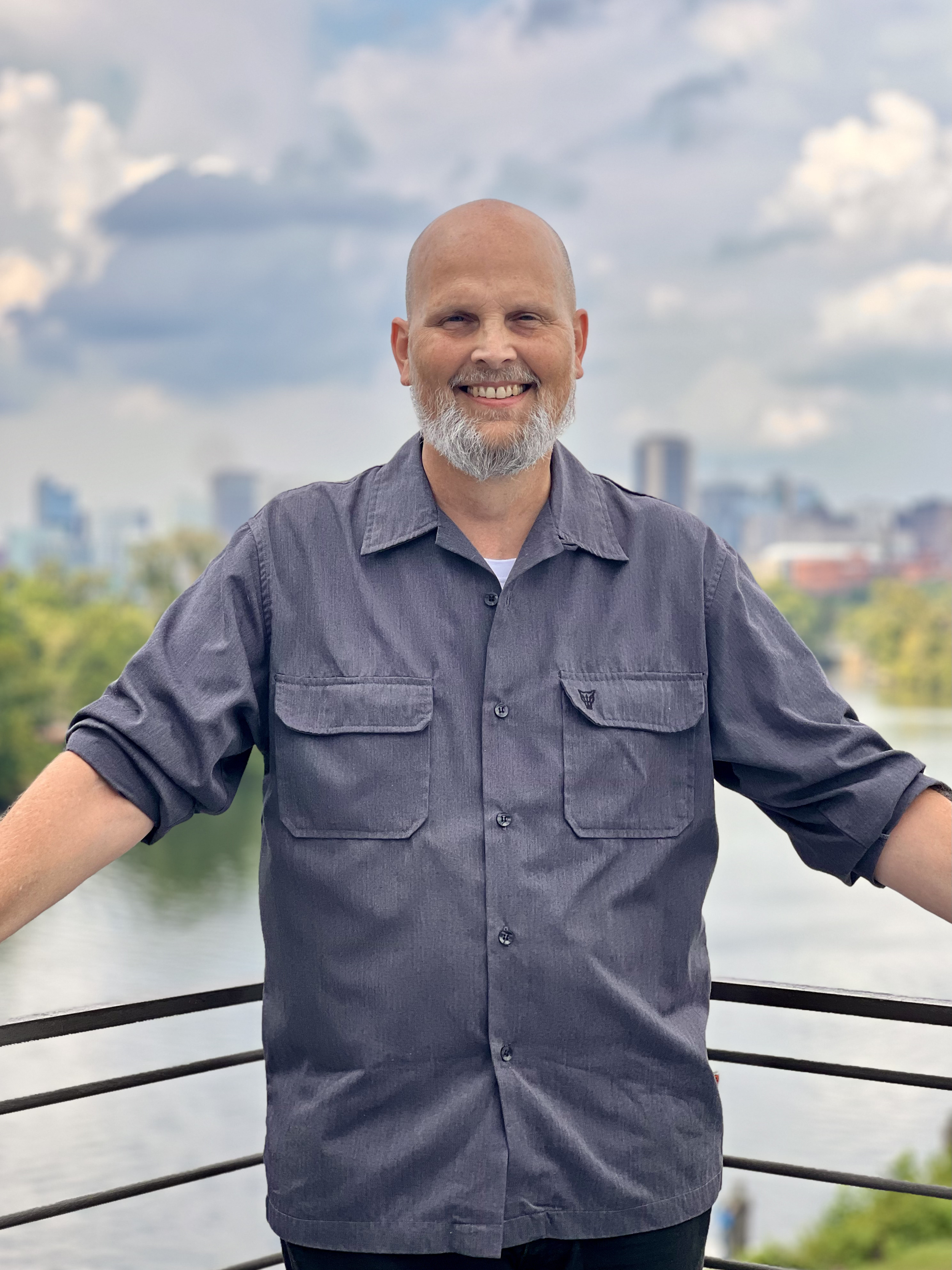 White man standing before a riverfront view of a city on a sunny day