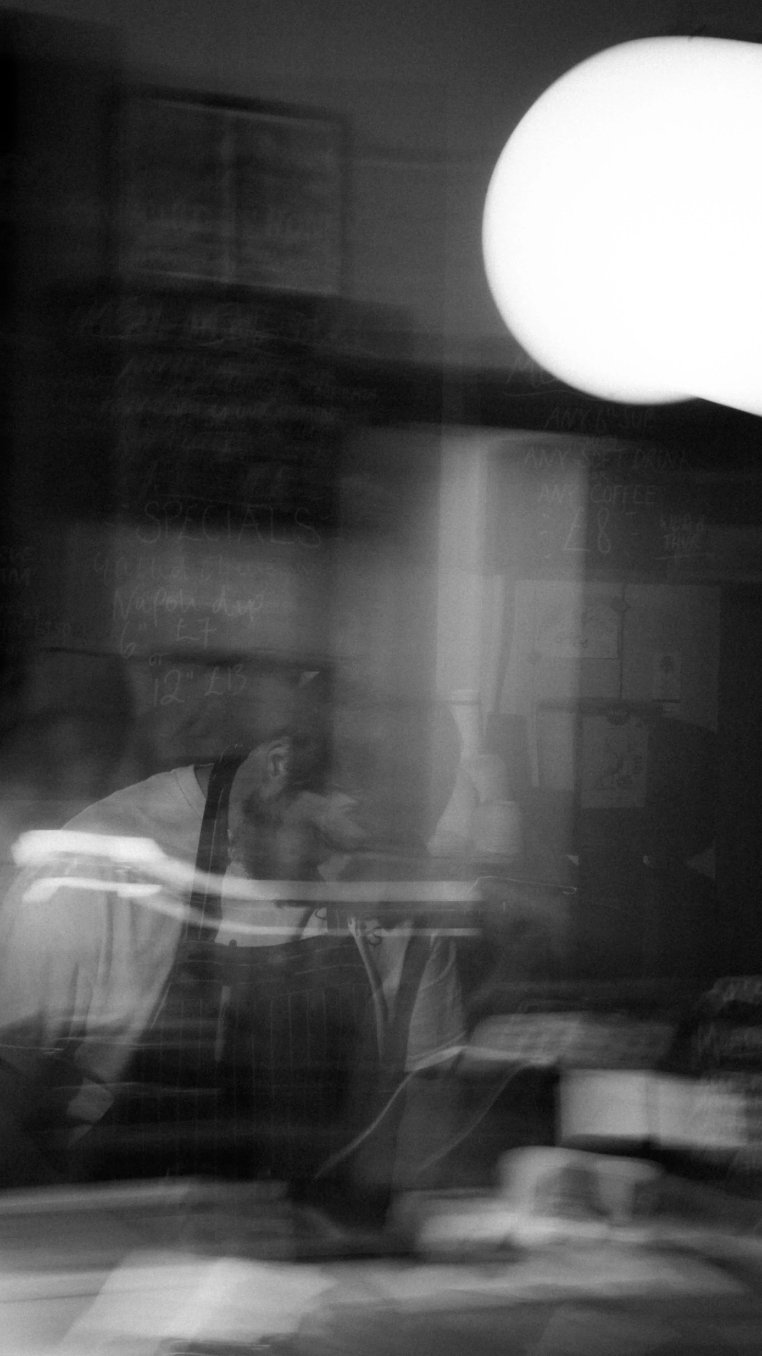 Black and white photo of reflection of a man working in a mirror, with a reflection of a bright light and blurred background.