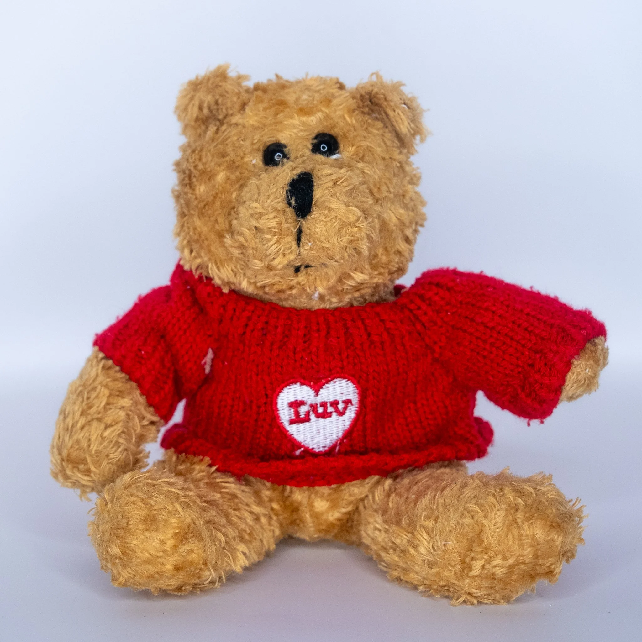 Straw coloured scruffy teddy with red knitted jumper. Red jumper has word 'luv' embroidered on it. Preloved toy but better than new from Irish social enterprise, Toys Arís